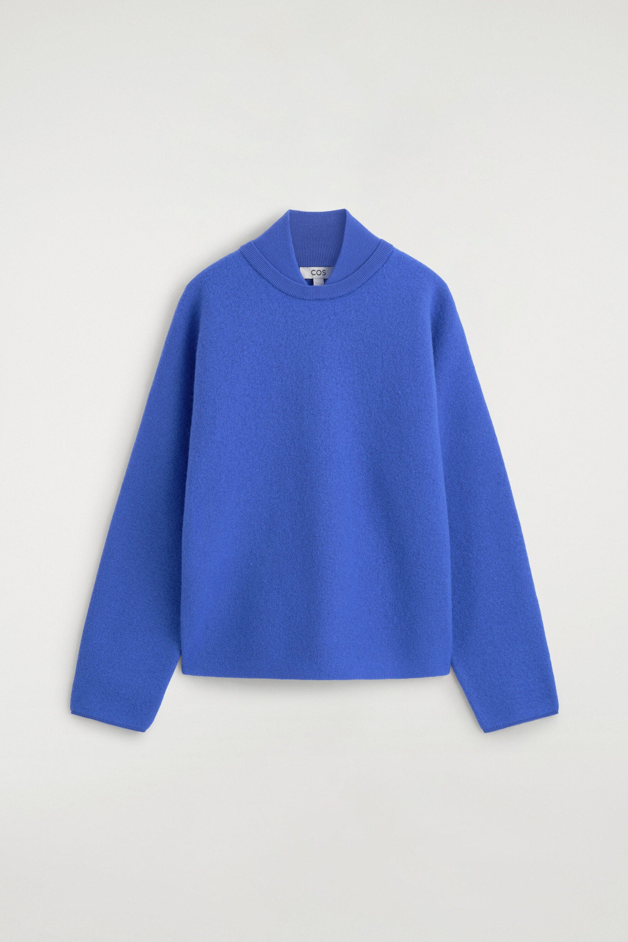 Le pull en laine bouillie bleu royal présente une silhouette décontractée et carrée en vue de face, avec un col superposé unique et un insert de faux col roulé côtelé. Le vêtement met en valeur de longues manches larges et un ourlet net sans bord-côte.