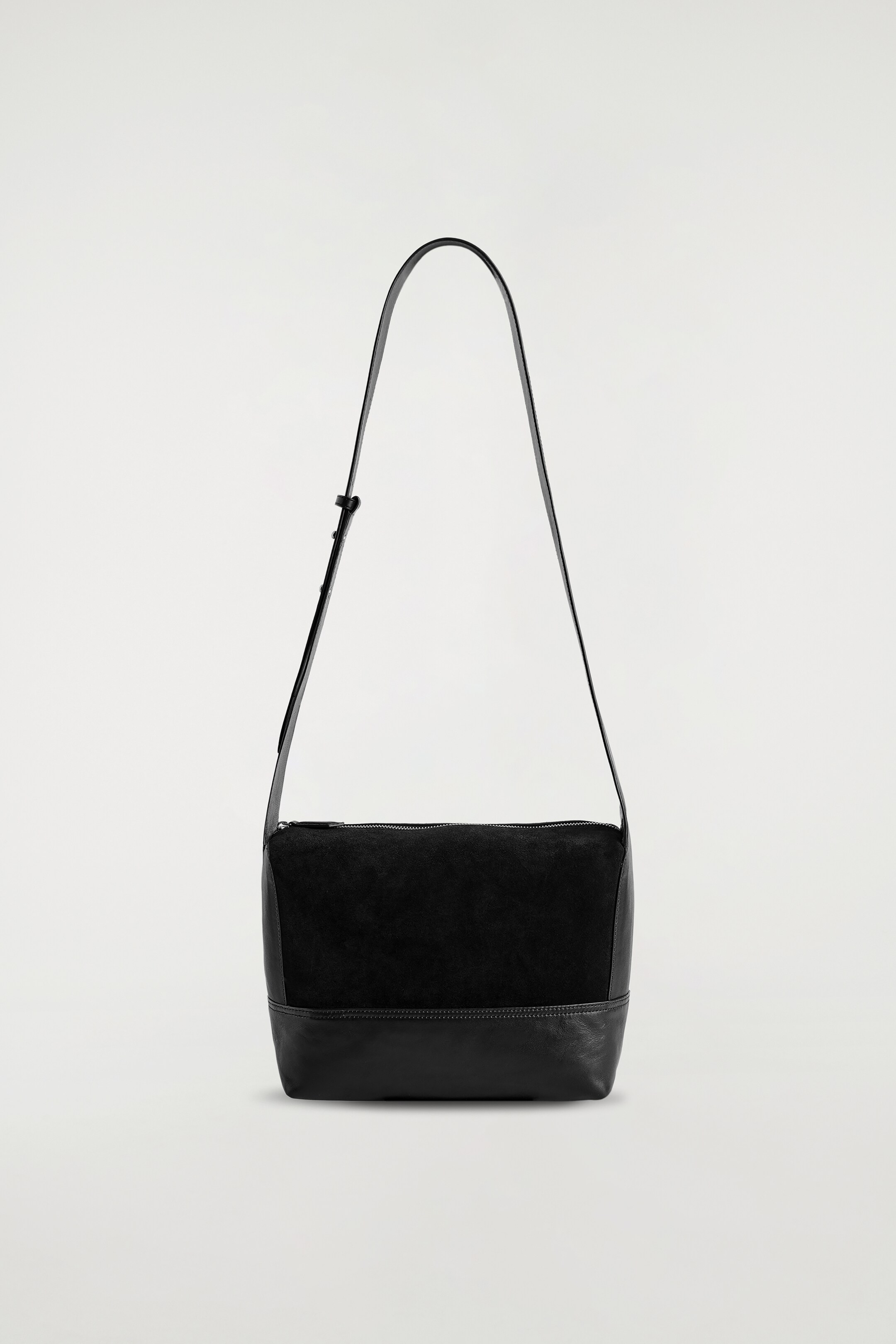 Visualizza immagine più grande: Una borsa compatta nera mostra la sua parte ANTERIORE, con una porzione superiore in camoscio e una base strutturata in pelle. È progettata con una chiusura superiore a zip e un unico cinturino regolabile in pelle nera.