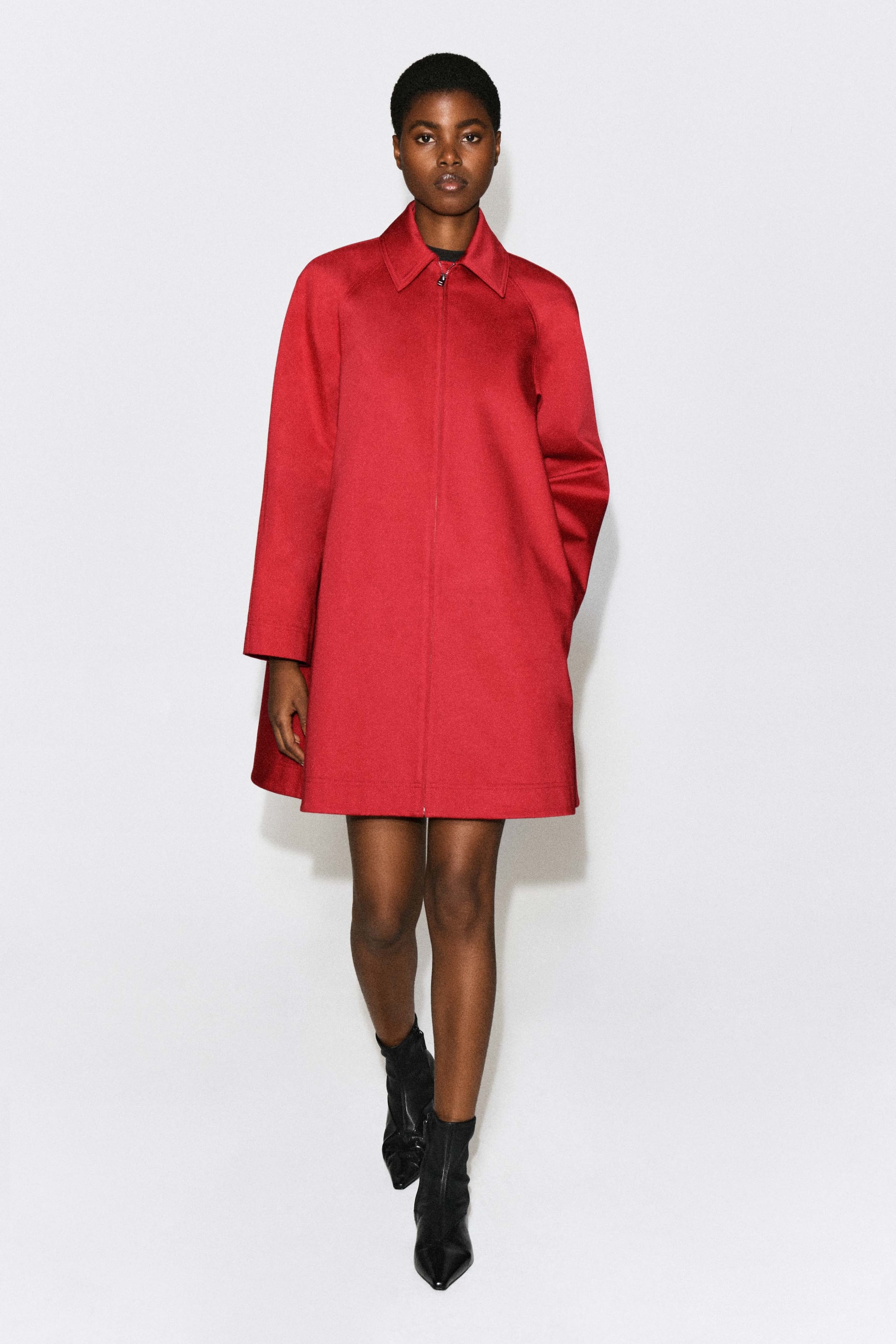 Agrandir l'image: Ce manteau swing sculptural rouge en coton, doté d’un col pointu, de manches longues et d’une silhouette structurée en ligne A, est porté par le mannequin. Le manteau est associé à des bottines noires à bout pointu.