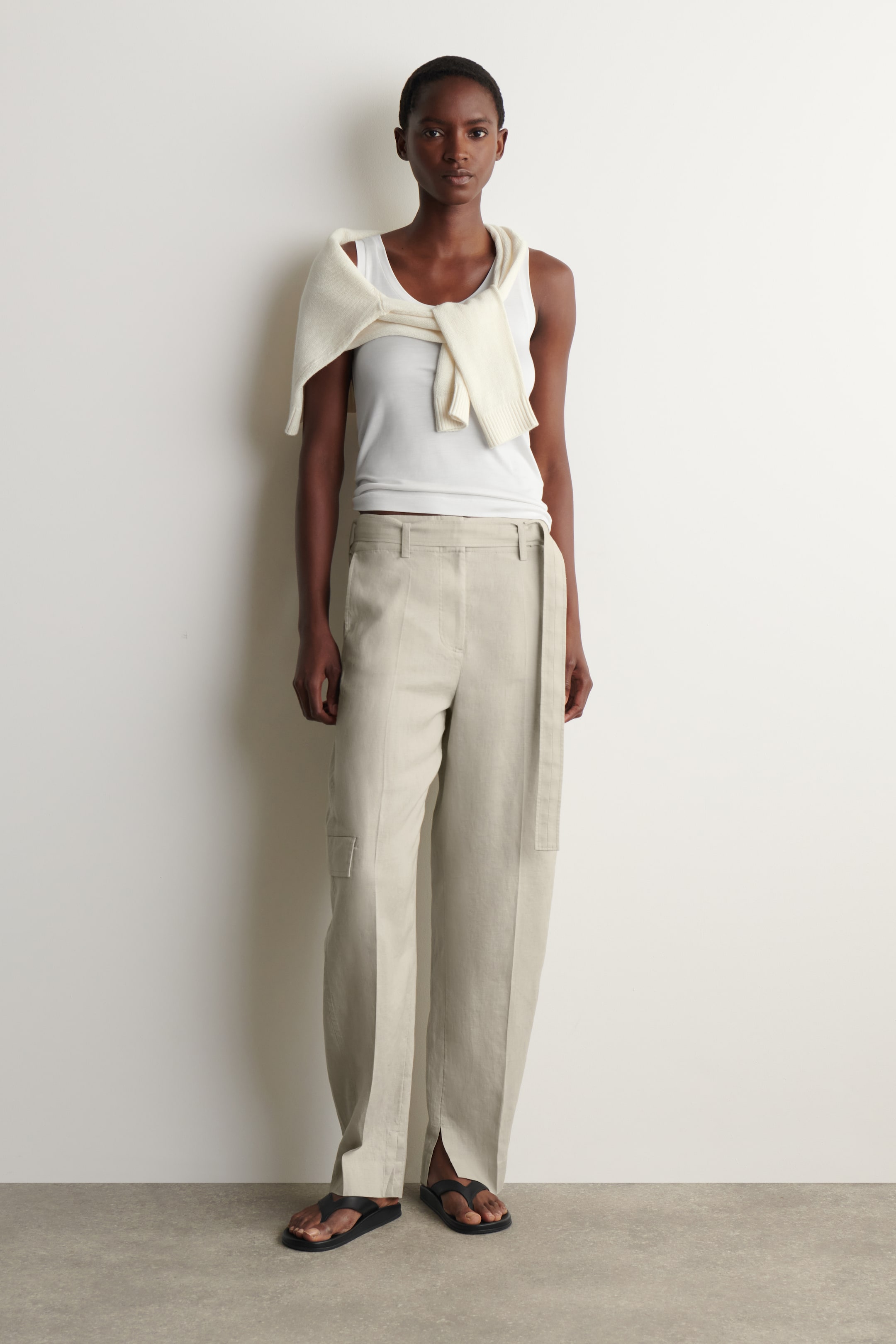 Agrandir l'image: Pantalon large beige clair avec une coupe taille haute, doté de passants de ceinture et d'une longue ceinture en tissu assortie tombant sur le côté droit. Une petite poche cargo carrée est visible sur la cuisse gauche, et les jambes du pantalon se terminent par des ourlets fendus aux chevilles, offrant une vue de face.