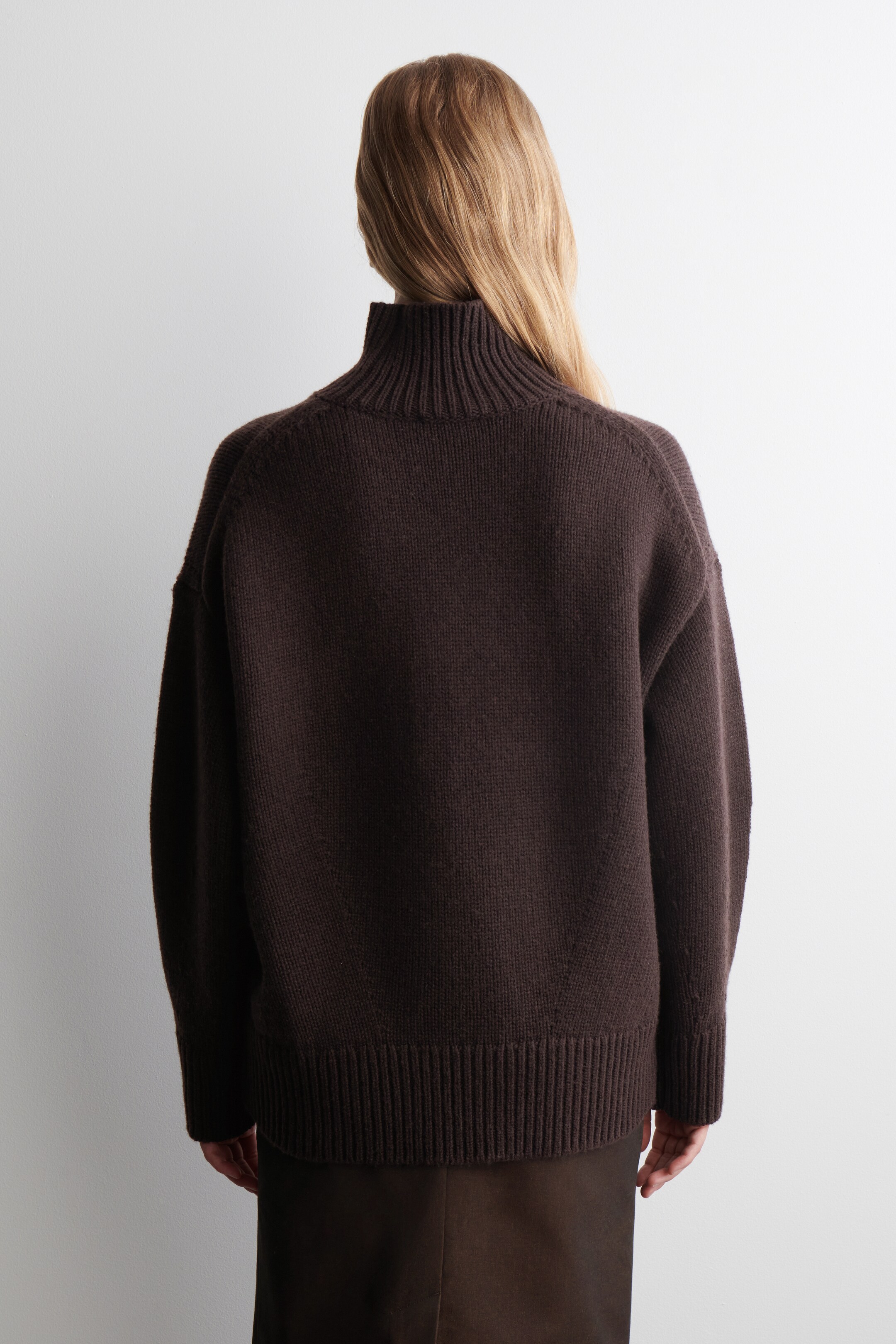 View larger image: A dark brown sweater is being shown from the back. It is featuring a high, ribbed turtleneck collar, long raglan sleeves, and a ribbed hem. The sweater is presenting a relaxed, oversized fit.