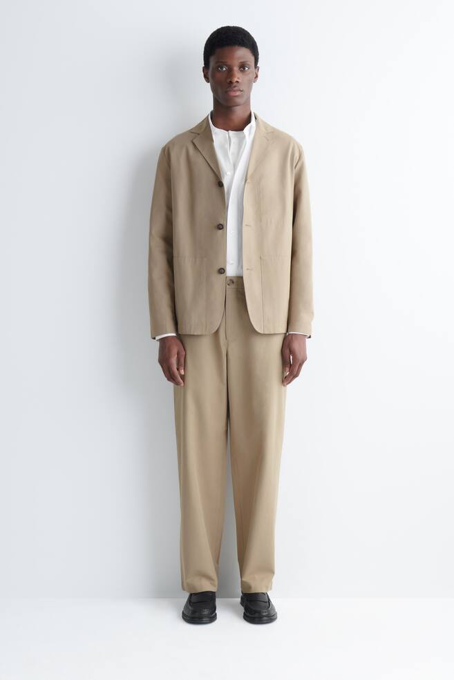 El modelo lleva pantalones chinos beige de pierna recta. Se combinan con una chaqueta beige a juego y una camisa blanca con cuello. - 1