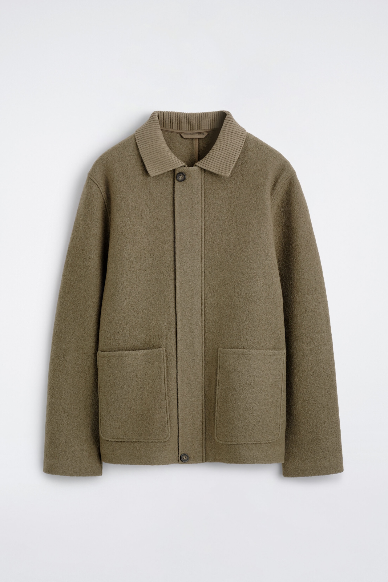 A boiled-wool chore jacket in an olive-brown hue is hanging in a front-facing view, showcasing a ribbed knit collar and a concealed button placket. The jacket features two large square patch pockets on the lower front and straight, clean-finished sleeves.