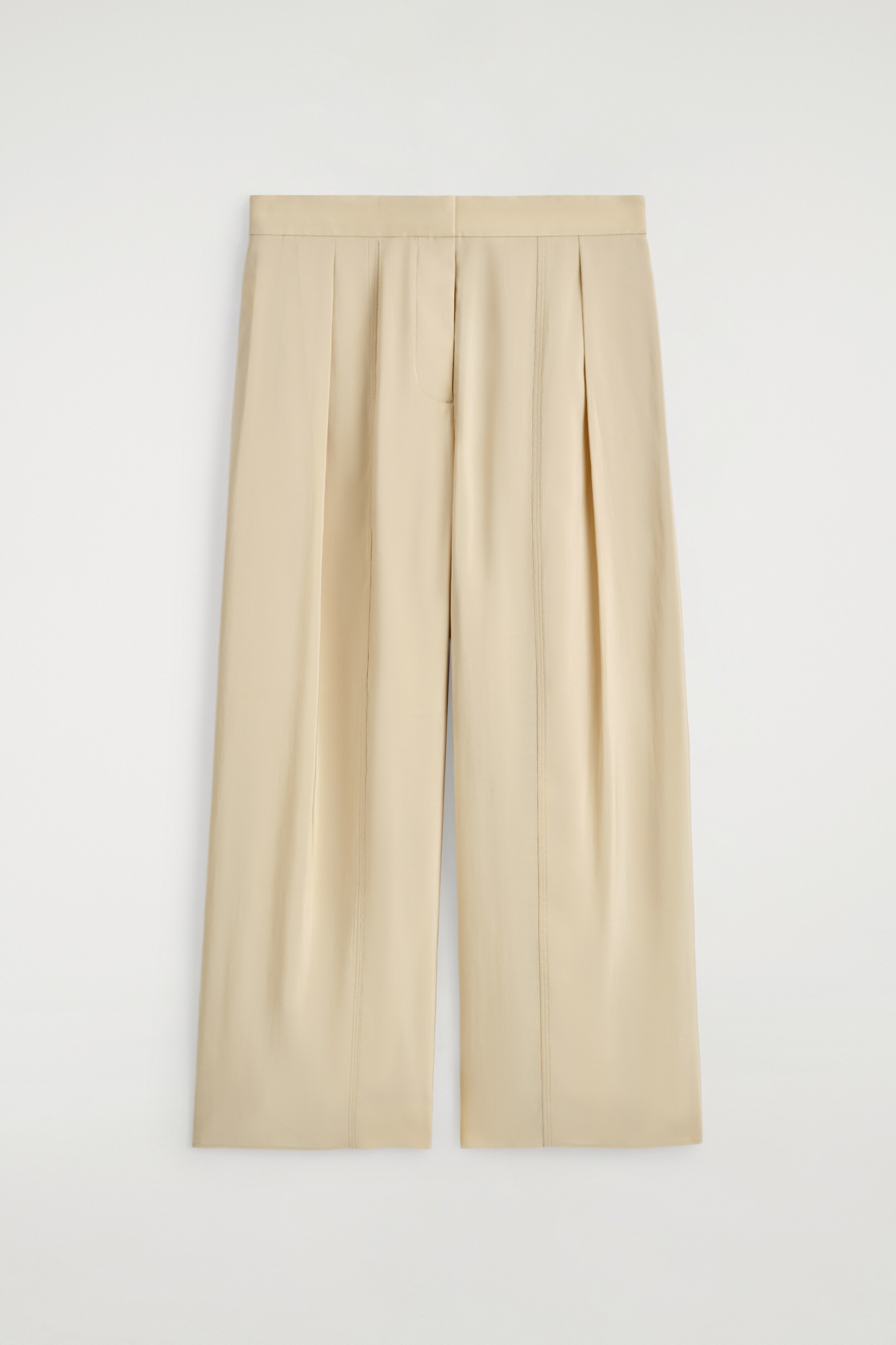 Zobacz większy obraz: FLUID PLEATED CULOTTES są pokazane od przodu, w jasnobeżowej płynnej tkaninie, z podwójnymi plisami w talii. Pionowe przeszycia biegną w dół każdej szerokiej, przyciętej nogawki, z widoczną kieszenią z rozcięciem na lewym przodzie.