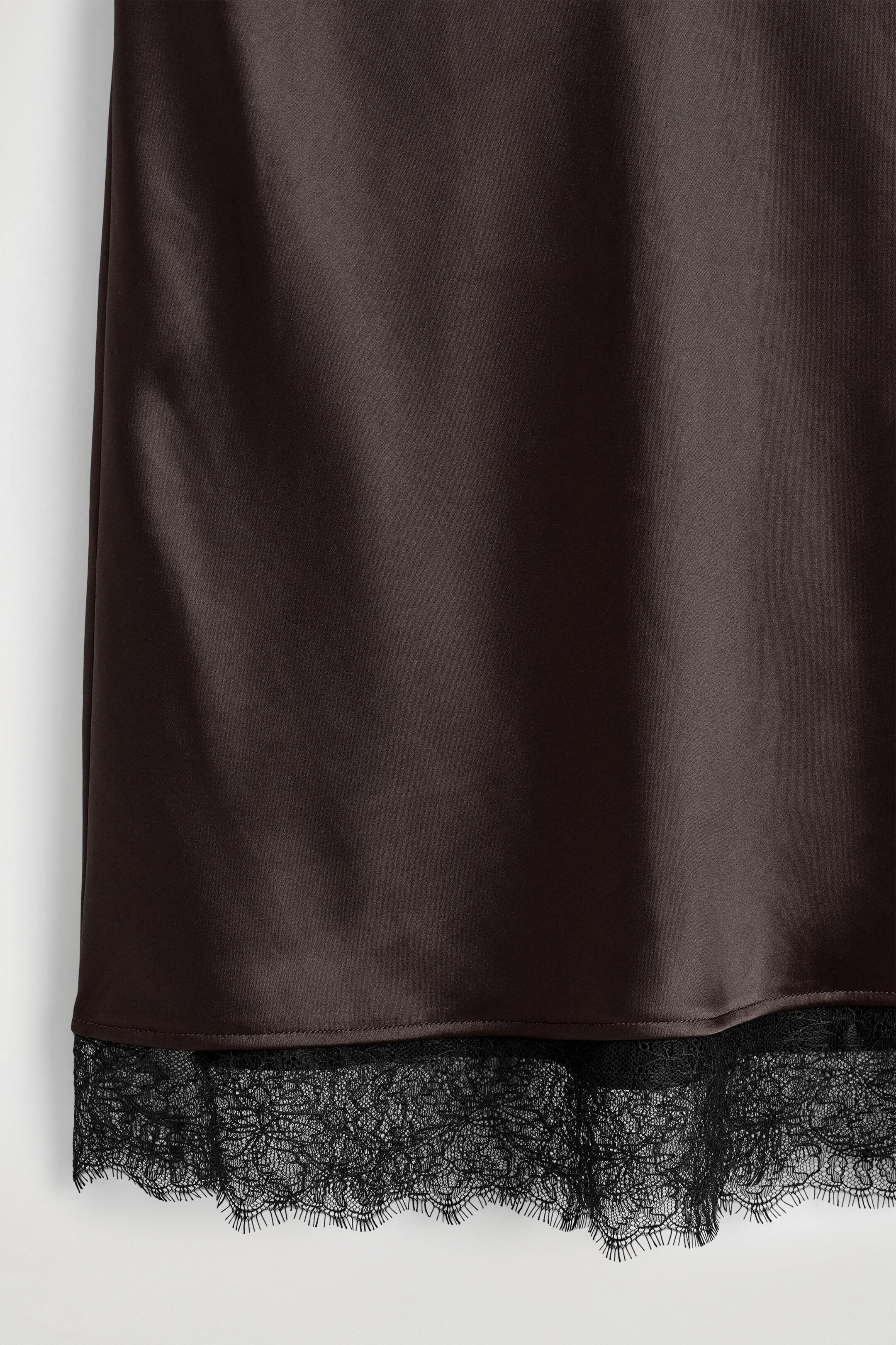 View larger image: The dark brown satin skirt is featuring a smooth, shimmering fabric and a delicate black lace trim with an intricate pattern along its lower edge.