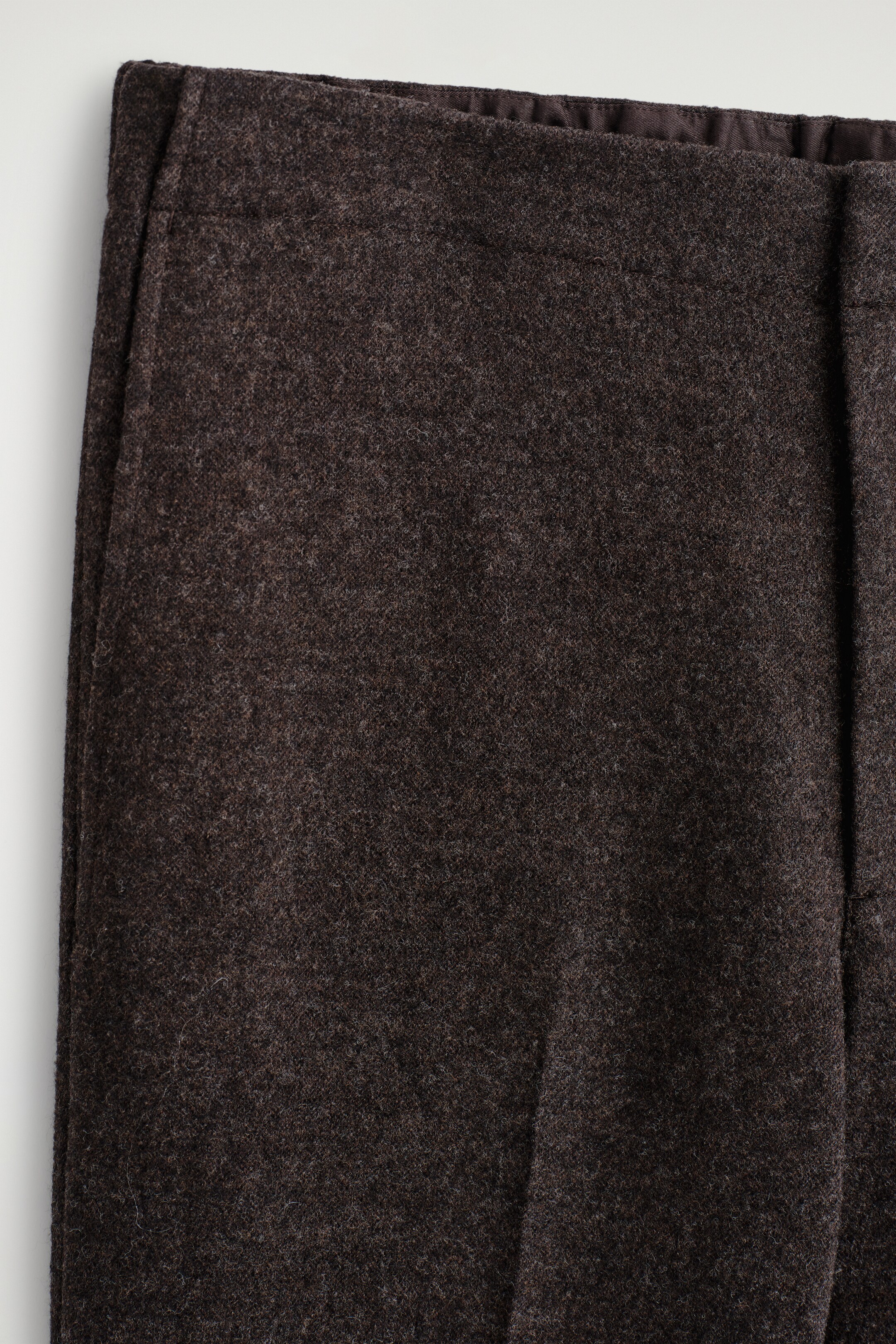 Agrandir l'image: Un pantalon brun foncé est présenté de face, avec une ceinture plate et un tissu texturé et moucheté. Une doublure brun foncé est visible le long du bord intérieur de la ceinture.