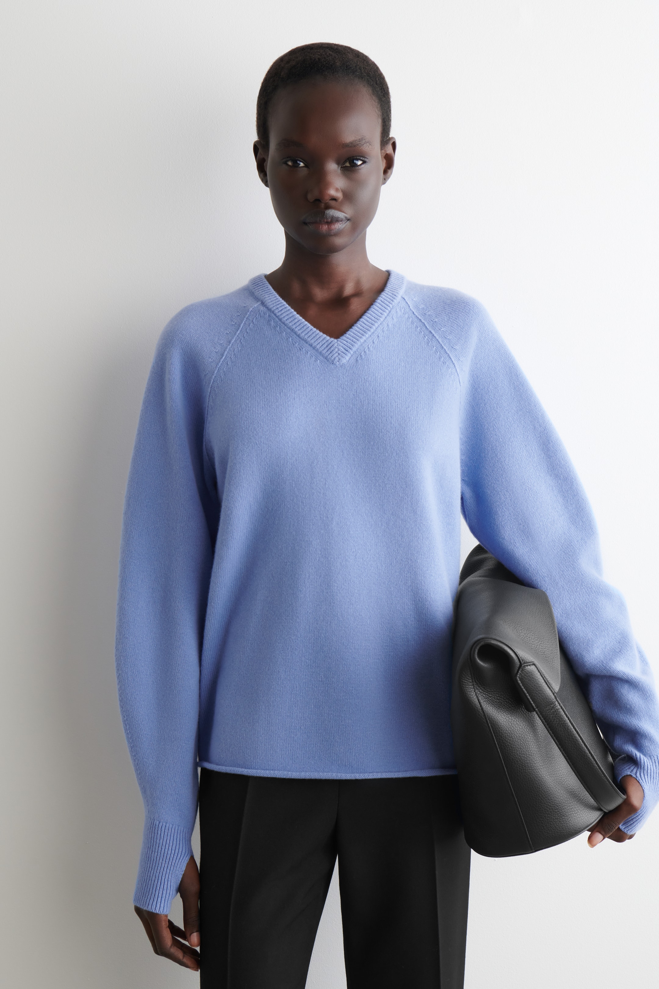 Visualizza immagine più grande: Un maglione azzurro con scollo a V è presentato frontalmente, caratterizzato da una vestibilità rilassata e uno scollo a V. Presenta maniche lunghe raglan con polsini a coste, uno dei quali include un foro per il pollice visibile.