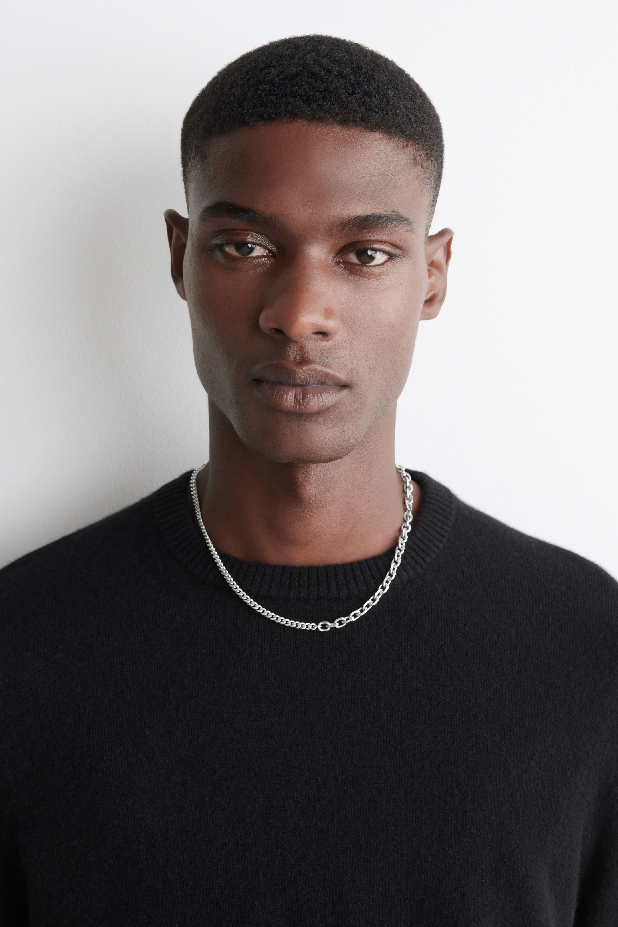 View larger image: A silver-toned chain necklace is combining a finer curb chain and a larger oval-link chain, with the two distinct styles visibly joining in the center. The necklace is resting on a black sweater, and it is visible from the front.