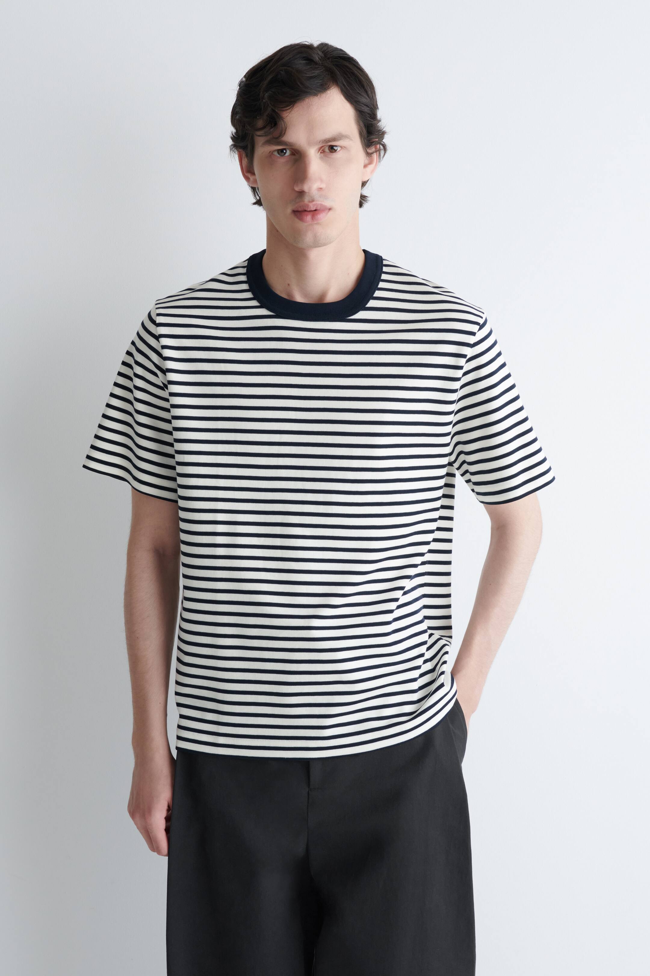 View larger image: A men's T-shirt is showcased from the front, featuring a cream base with horizontal navy blue stripes. It is designed with a ribbed navy crew neck and short sleeves, offering a relaxed fit.