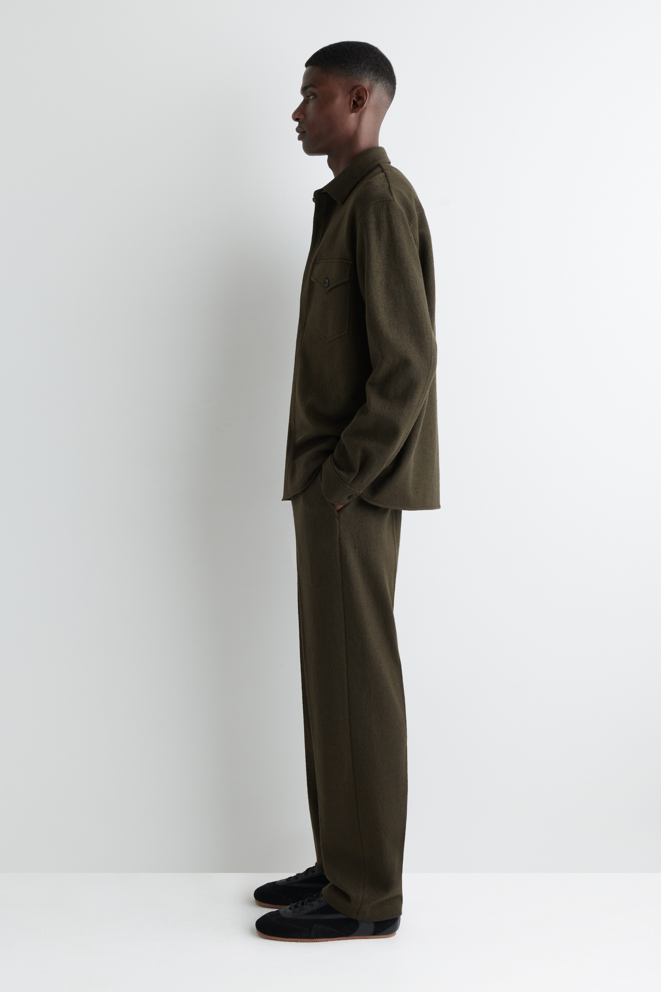Agrandir l'image: Un ensemble de chemise et pantalon vert olive assorti est présenté en vue de profil latéral. La chemise à coupe décontractée présente un col pointu et deux poches poitrine à rabat, tandis que le pantalon est conçu avec une silhouette droite et décontractée.