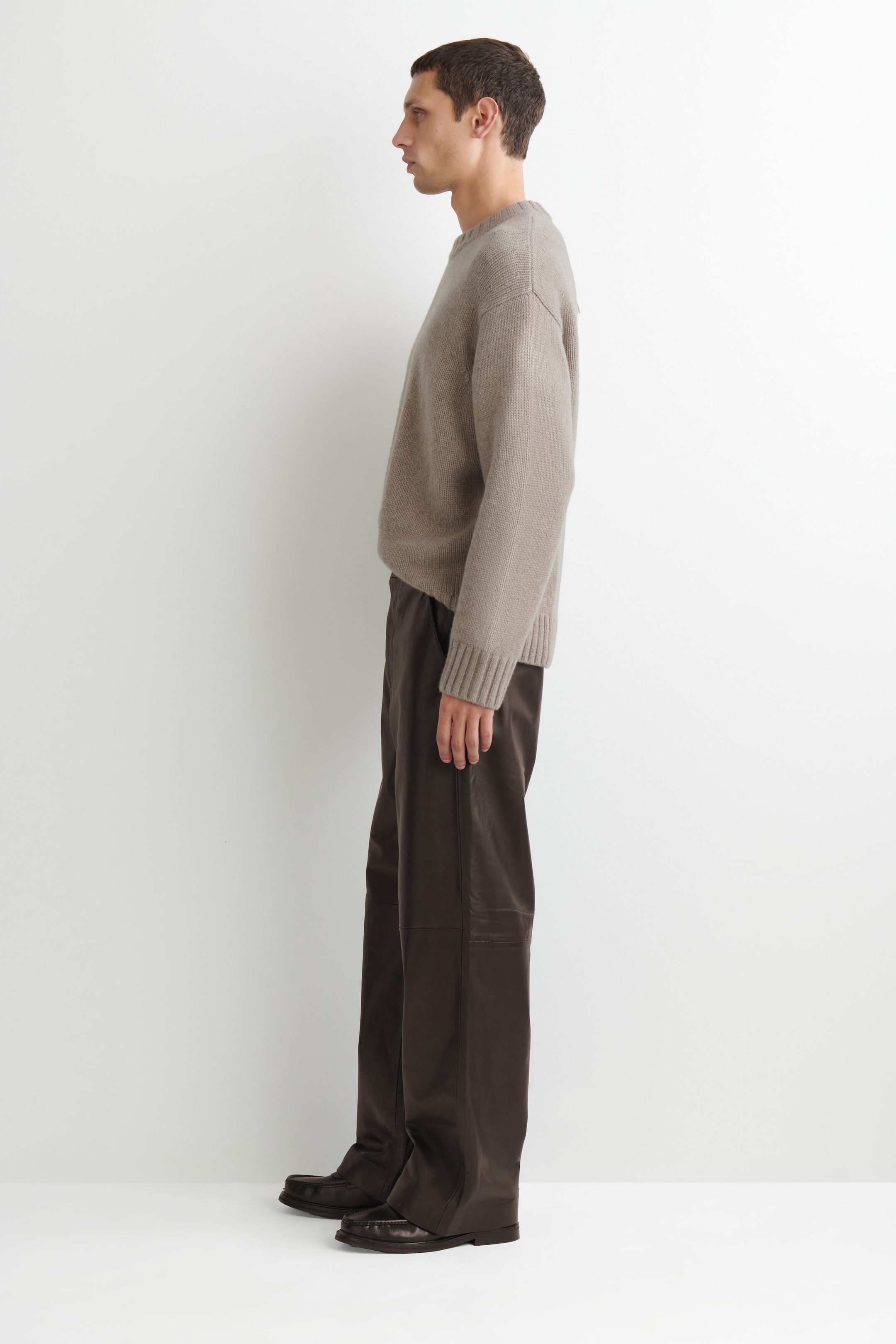 These dark brown leather relaxed-fit straight-leg pants drape in a loose, straight-leg silhouette, shown from a left-facing profile view. The pants feature a horizontal seam detail across the knee and pool slightly over dark brown leather loafers. These dark brown leather relaxed-fit straight-leg pants drape in a loose, straight-leg silhouette, shown from a left-facing profile view. The pants feature a horizontal seam detail across the knee and pool slightly over dark brown leather loafers.