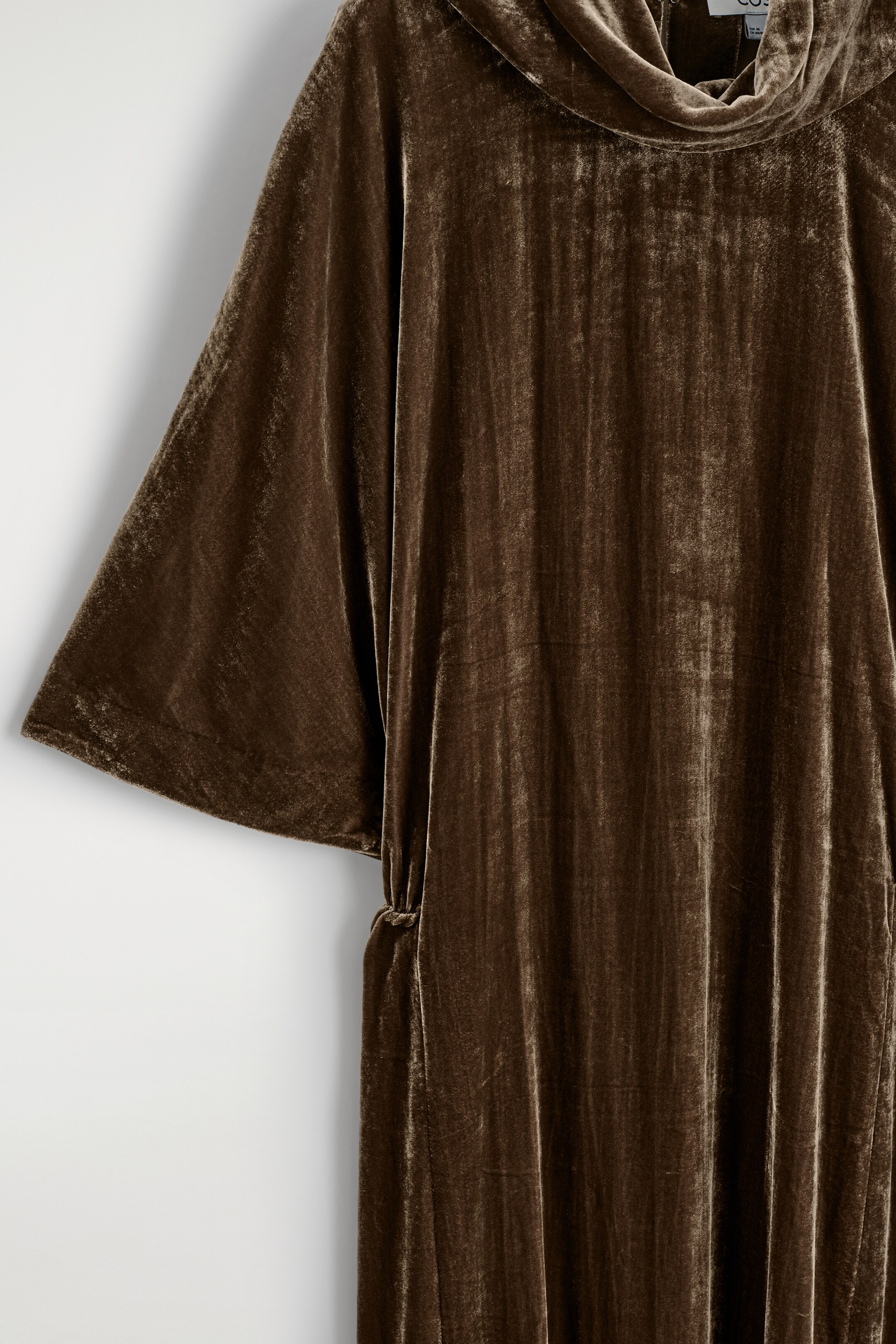 Grösseres Bild ansehen: Ein bronze-braunes Samtkleid weist einen drapierten Trichterkragen, weite Fledermausärmel und ein elastisches Blouson-Taille-Detail auf, das an der Seite sichtbar ist.