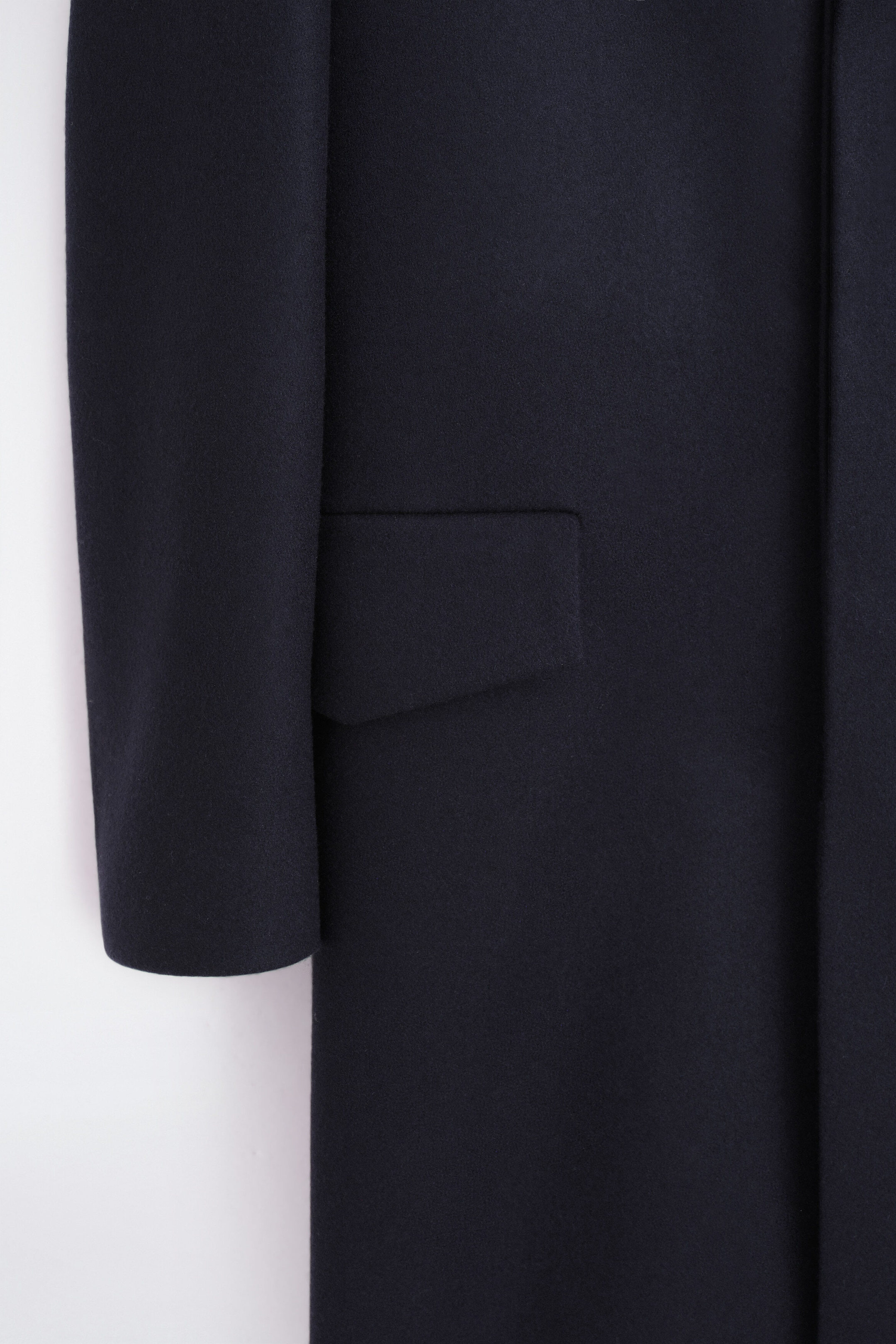 A dark blue coat is being shown, featuring a long sleeve on the left side and a rectangular flap pocket on the main body. The coat’s smooth fabric displays a subtle, fine texture. A dark blue coat is being shown, featuring a long sleeve on the left side and a rectangular flap pocket on the main body. The coat’s smooth fabric displays a subtle, fine texture.