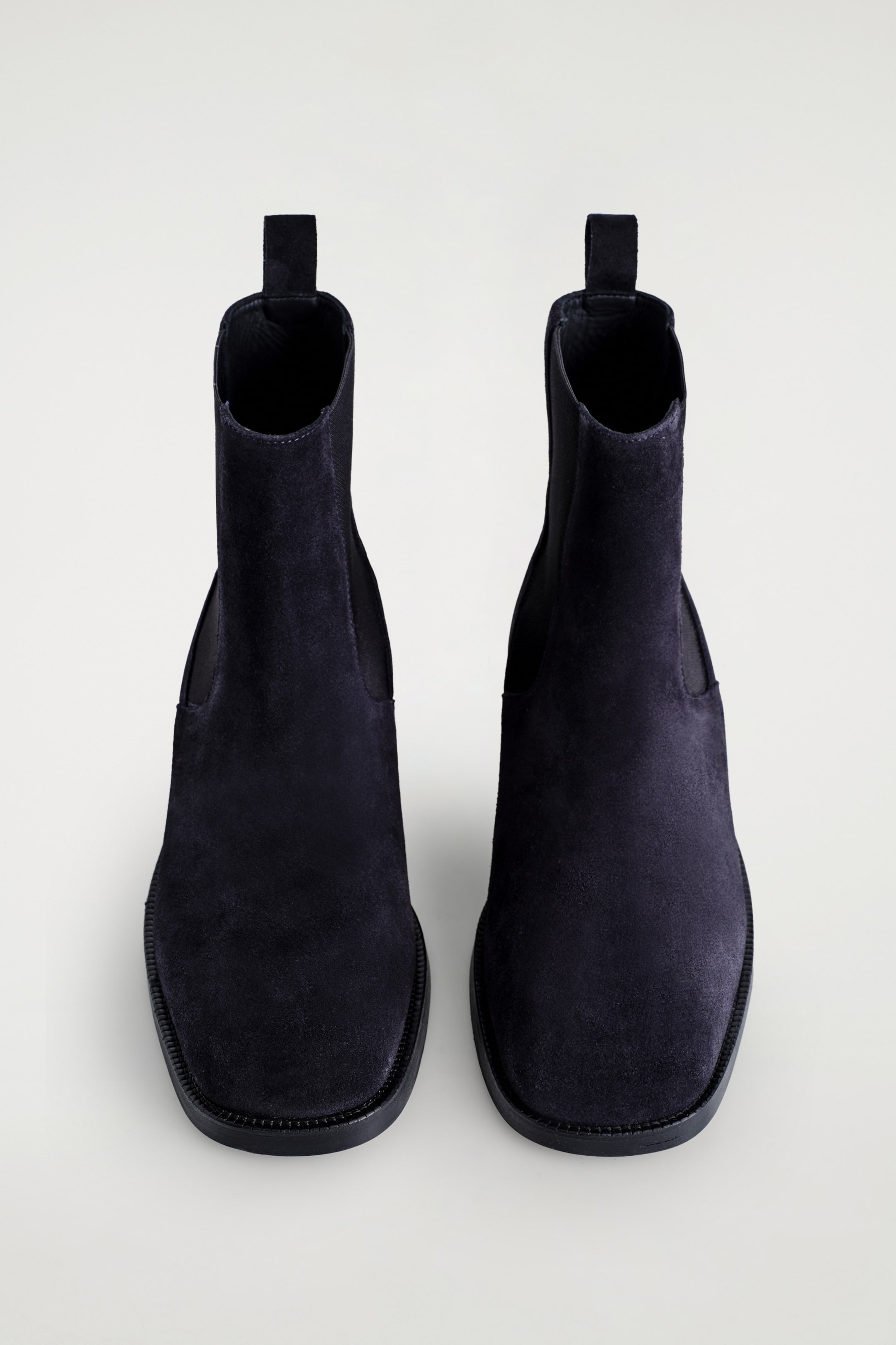 Agrandir l'image: Deux bottines Chelsea en daim foncé sont présentées en vue de dessus, avec des bouts carrés, des inserts élastiques sur les côtés et des languettes à l'arrière.
