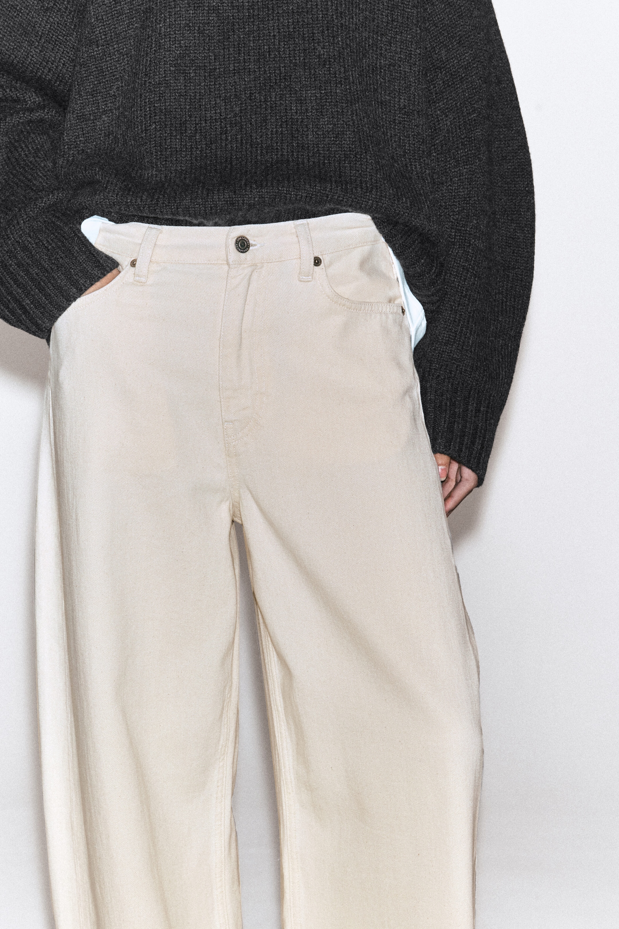 The Lagoon wide-leg jeans are crafted from cream-coloured denim and shown from the front, featuring a high-rise waist with belt loops, a button fastening, and classic scoop pockets. A dark grey knit jumper is tucked into the waistband, highlighting the relaxed, wide-leg fit of the jeans. The Lagoon wide-leg jeans are crafted from cream-coloured denim and shown from the front, featuring a high-rise waist with belt loops, a button fastening, and classic scoop pockets. A dark grey knit jumper is tucked into the waistband, highlighting the relaxed, wide-leg fit of the jeans.