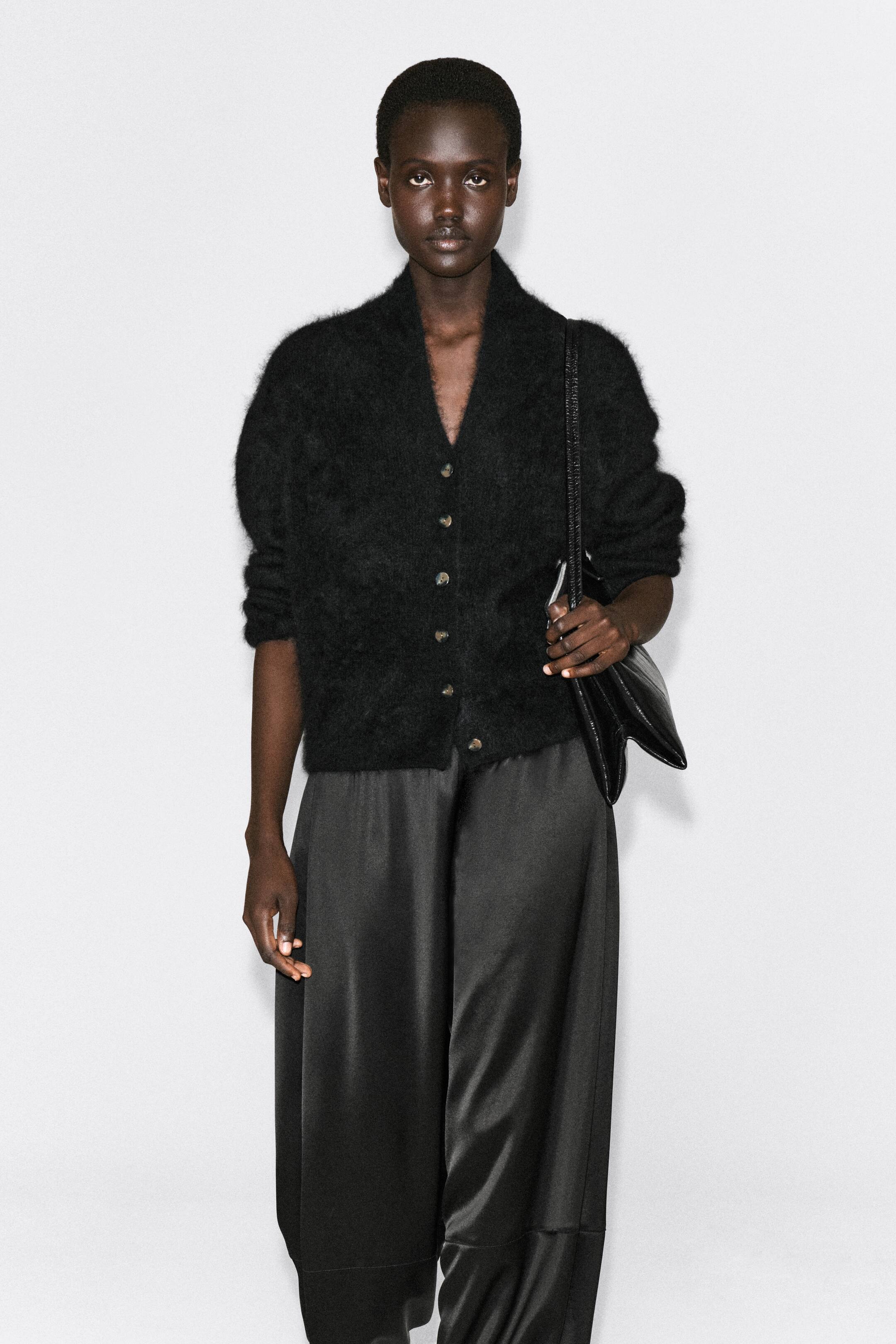 Agrandir l'image: Le cardigan en laine mérinos brossée drapée est présenté de face, avec un tricot noir, duveteux et texturé, un col drapé façon châle et une fermeture boutonnée sur le devant. Le cardigan est porté boutonné, avec ses manches à la coupe décontractée légèrement remontées sur les bras.