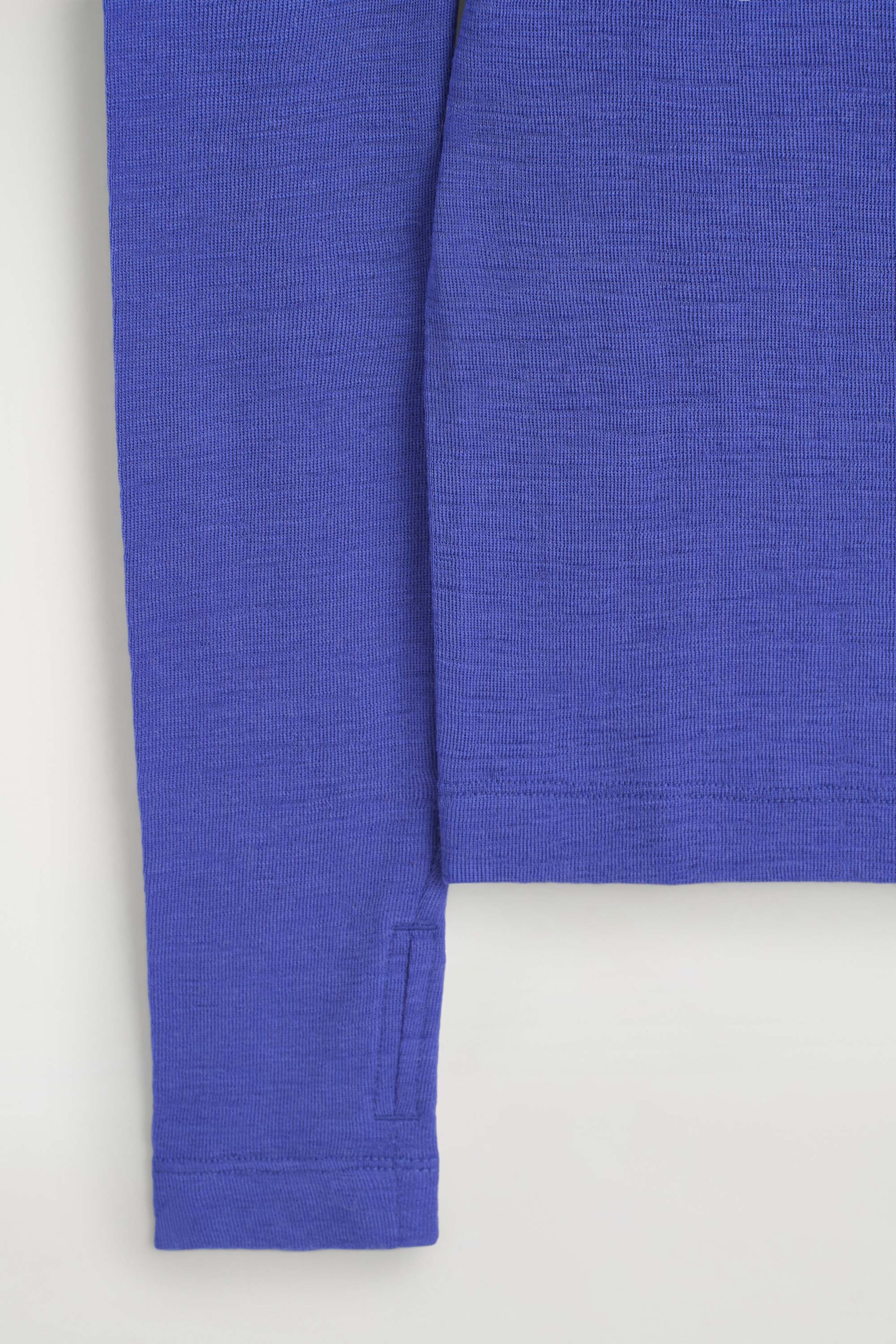 The slim merino wool top showcases its vibrant blue, fine-knit texture in a close-up view. The long sleeve features a stitched thumbhole detail near the cuff, hanging parallel to the straight hem of the bodice. The slim merino wool top showcases its vibrant blue, fine-knit texture in a close-up view. The long sleeve features a stitched thumbhole detail near the cuff, hanging parallel to the straight hem of the bodice.