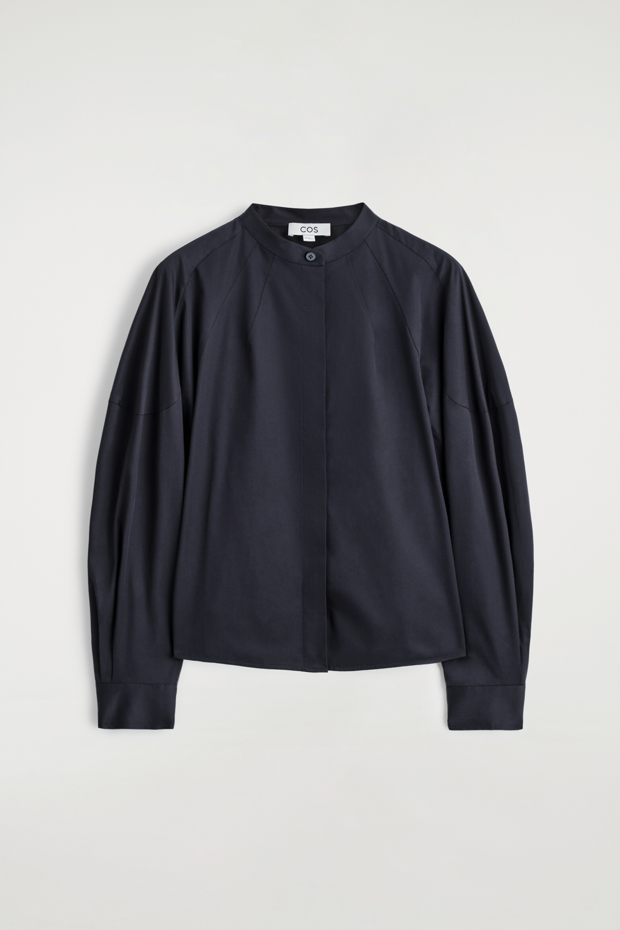 Agrandir l'image: Une chemise bleu foncé est orientée vers l'avant, avec un col rond sans col et une fermeture à bouton unique visible. Elle est conçue avec des manches raglan et des détails subtils de pinces sur le panneau avant.