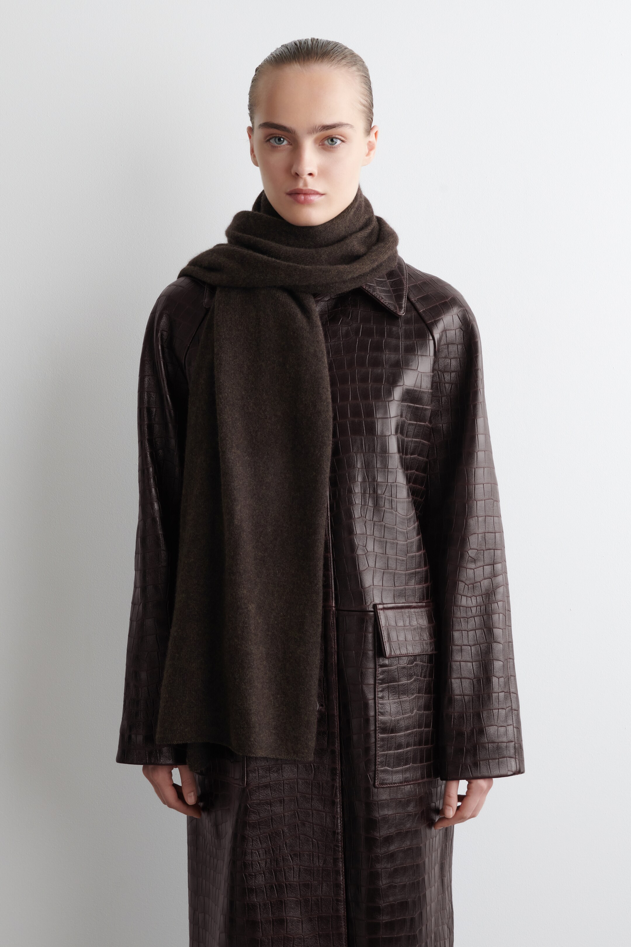 Agrandir l'image: Un manteau en cuir marron foncé à motif crocodile, avec de larges revers en pointe et une poche plaquée carrée sur le côté droit, est porté avec une écharpe marron foncé enroulée autour du cou, offrant une vue de face.