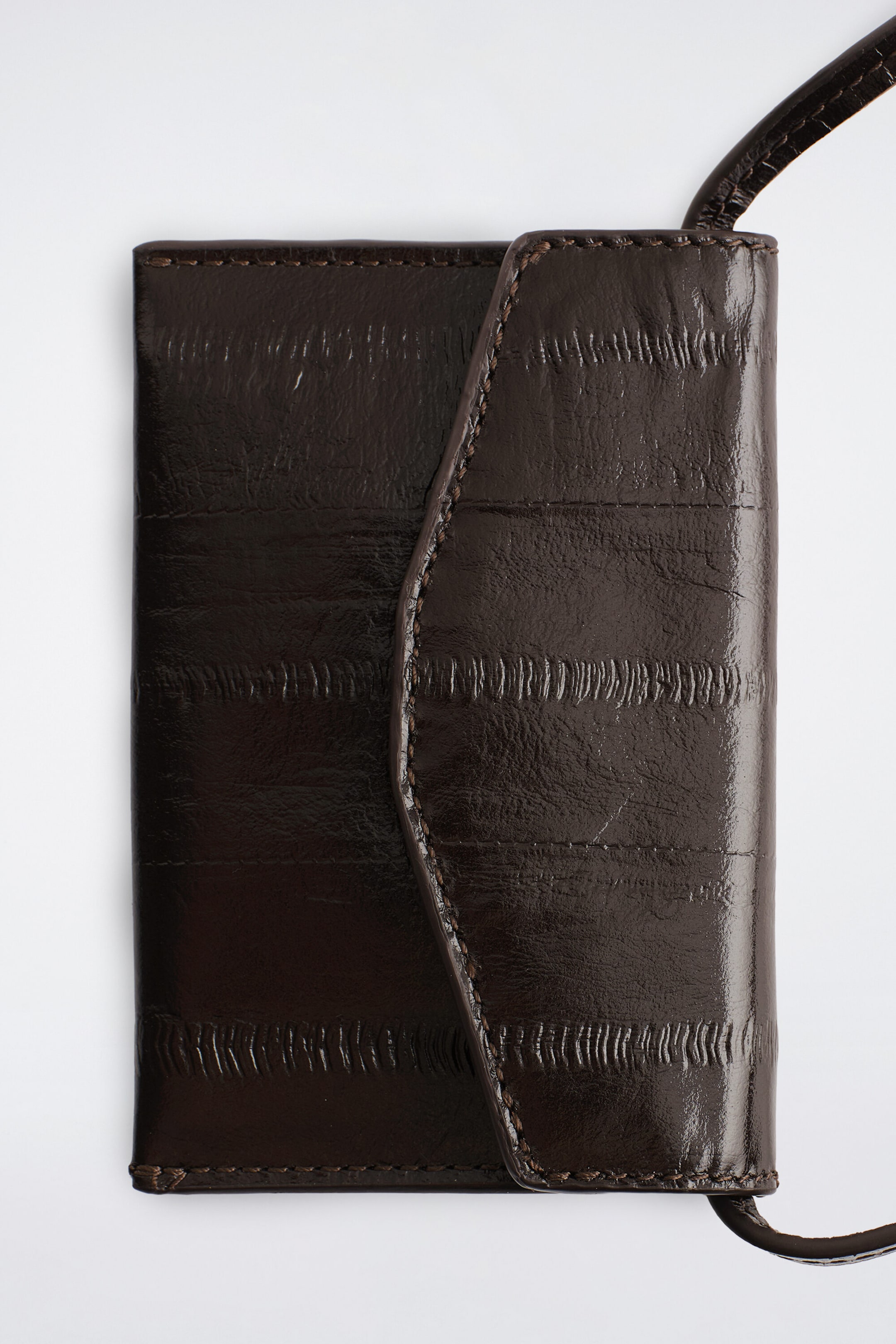 The dark brown eel-effect leather cardholder has a glossy finish, distinctive horizontal panels with textured ridges, and a curved fold-over flap with tonal topstitching. A thin, matching leather strap extends from the side of the cardholder. The dark brown eel-effect leather cardholder has a glossy finish, distinctive horizontal panels with textured ridges, and a curved fold-over flap with tonal topstitching. A thin, matching leather strap extends from the side of the cardholder.