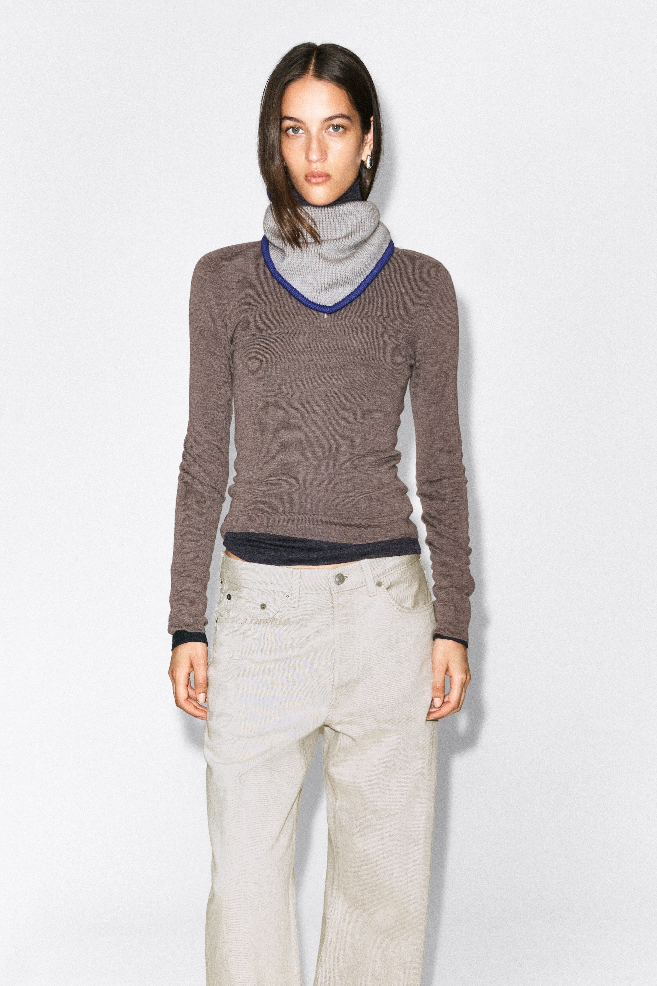 The contrast-tipped merino wool triangle scarf in light grey with a bright blue ribbed border is being worn around the model’s neck. The ribbed scarf is styled over a brown long-sleeve knit top, draped to form a pointed cowl shape. The contrast-tipped merino wool triangle scarf in light grey with a bright blue ribbed border is being worn around the model’s neck. The ribbed scarf is styled over a brown long-sleeve knit top, draped to form a pointed cowl shape.