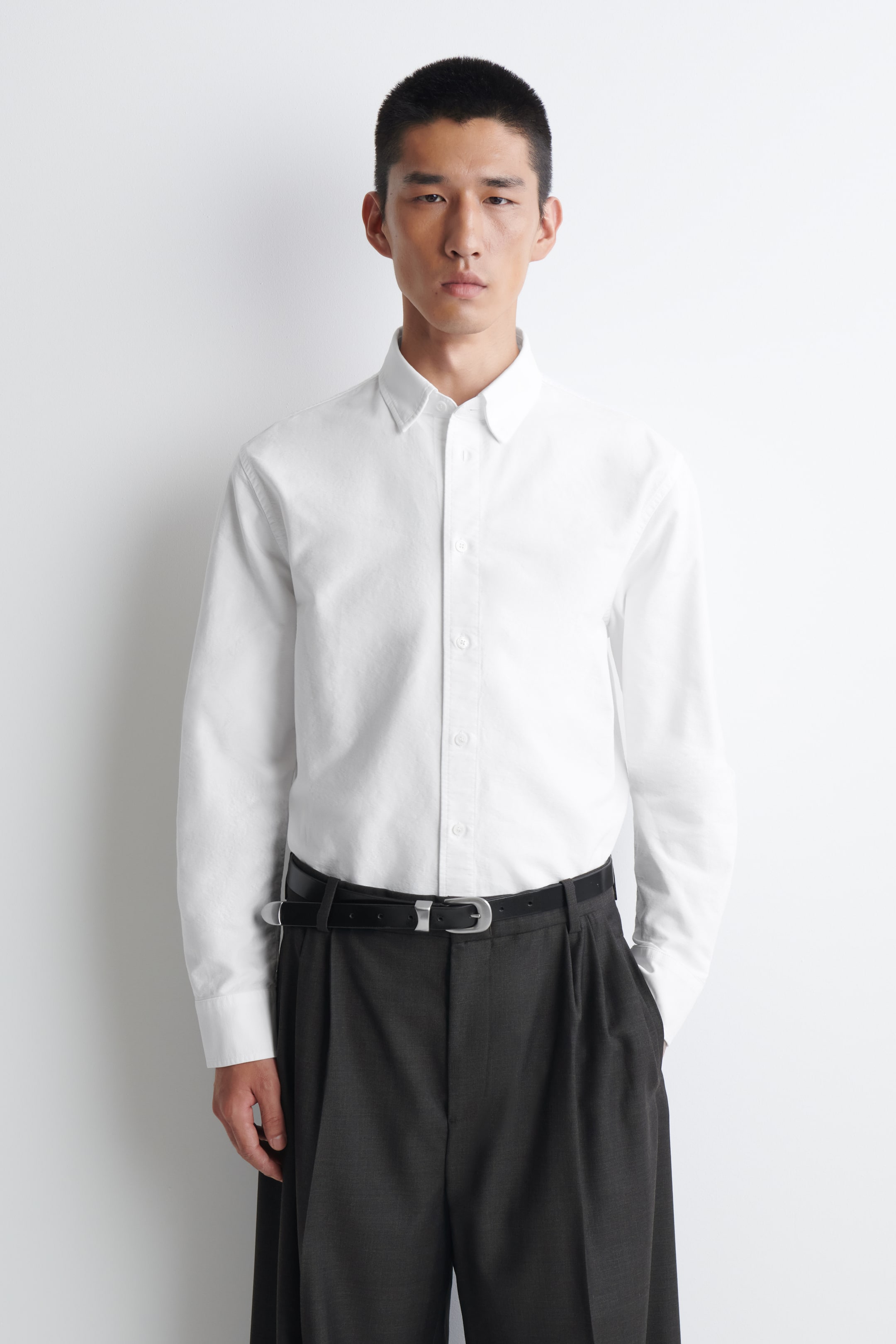Grösseres Bild ansehen: Ein weisses Oxford-Hemd mit Button-down-Kragen, einer durchgehenden Knopfleiste vorne und langen Ärmeln mit geknöpften Manschetten. Das Hemd hat eine lockere Passform und ist in die Hose gesteckt dargestellt.