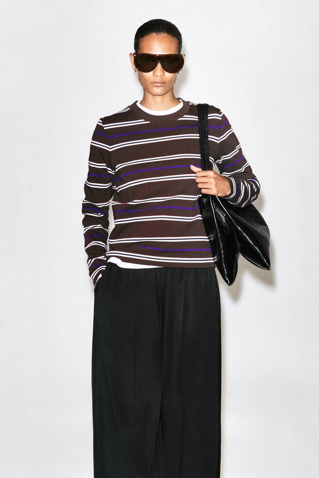 La modelo lleva una camiseta de manga larga de corte limpio con rayas horizontales en marrÃ³n, blanco y morado. La camiseta de rayas se lleva sobre una camiseta blanca de cuello redondo y se combina con un pantalÃ³n negro de pernera ancha, mientras que en un lado lleva un bolso negro de hombro. - 1