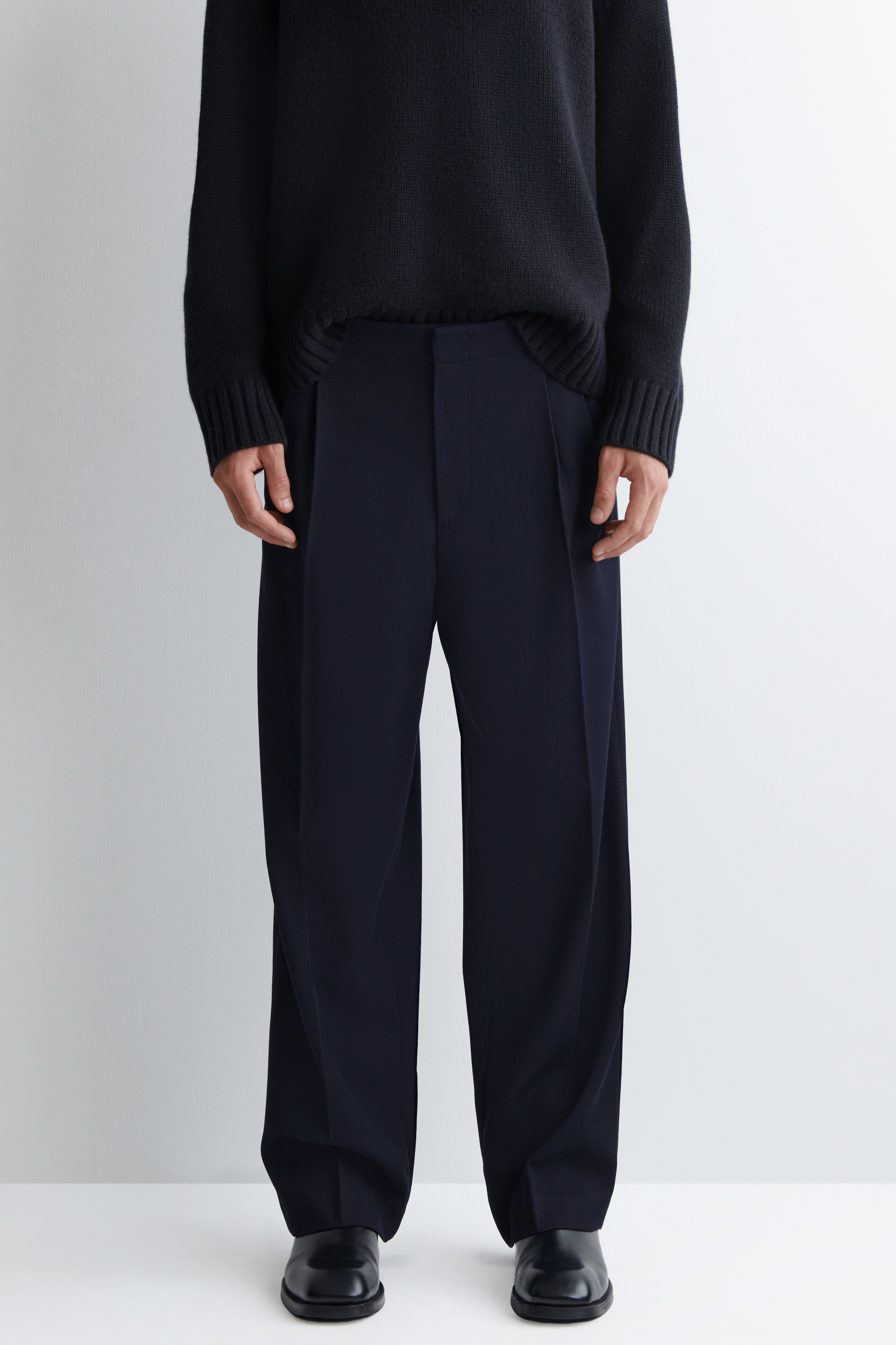Agrandir l'image: Un pantalon bleu foncé à jambes larges est présenté en pleine longueur, face à l'avant. Le pantalon présente une coupe décontractée avec des plis simples à la taille haute et tombe librement jusqu'au sol.