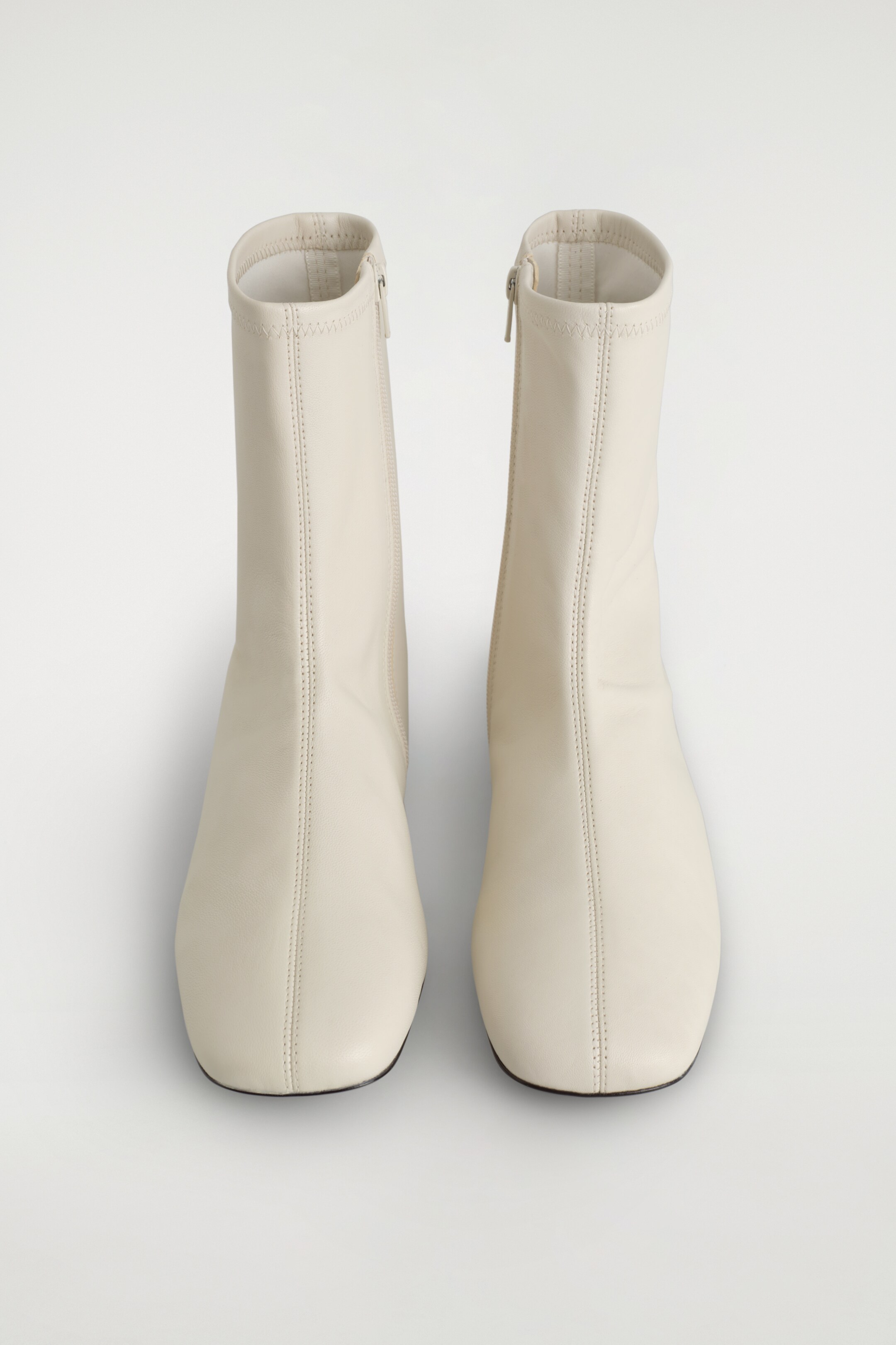 View larger image: A pair of neutral chalk leather sock boots is presented, featuring a slim silhouette with rounded square toes. Each boot is designed with a metal zip on the inner side of the shaft and a visible center seam running down the front.