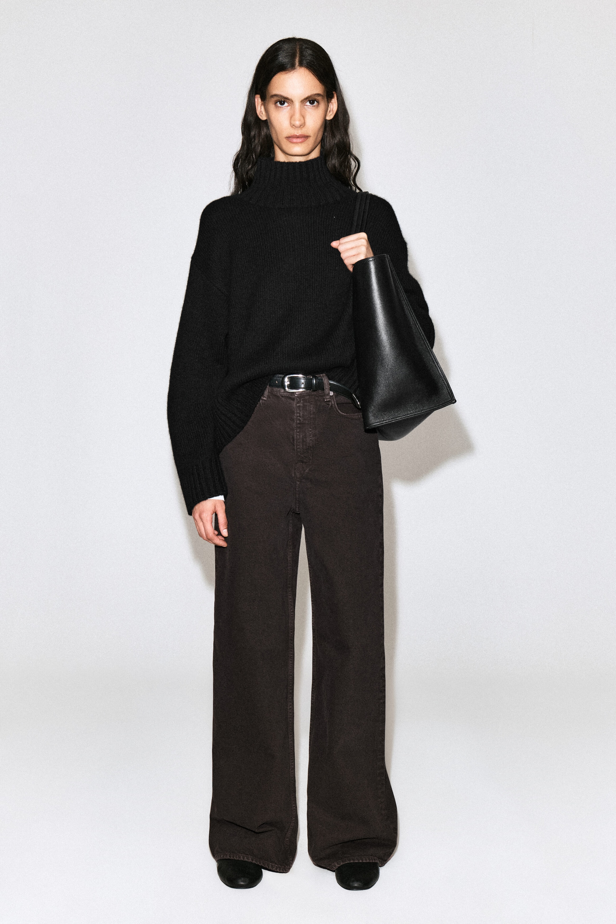 The model is wearing dial wide-leg jeans in a dark brown wash, featuring a high-rise waist and a relaxed, full-length wide-leg cut. The jeans are styled with a black leather belt threaded through the belt loops and a black knit turtleneck sweater, partially tucked into the front waistband. The model is wearing dial wide-leg jeans in a dark brown wash, featuring a high-rise waist and a relaxed, full-length wide-leg cut. The jeans are styled with a black leather belt threaded through the belt loops and a black knit turtleneck sweater, partially tucked into the front waistband.