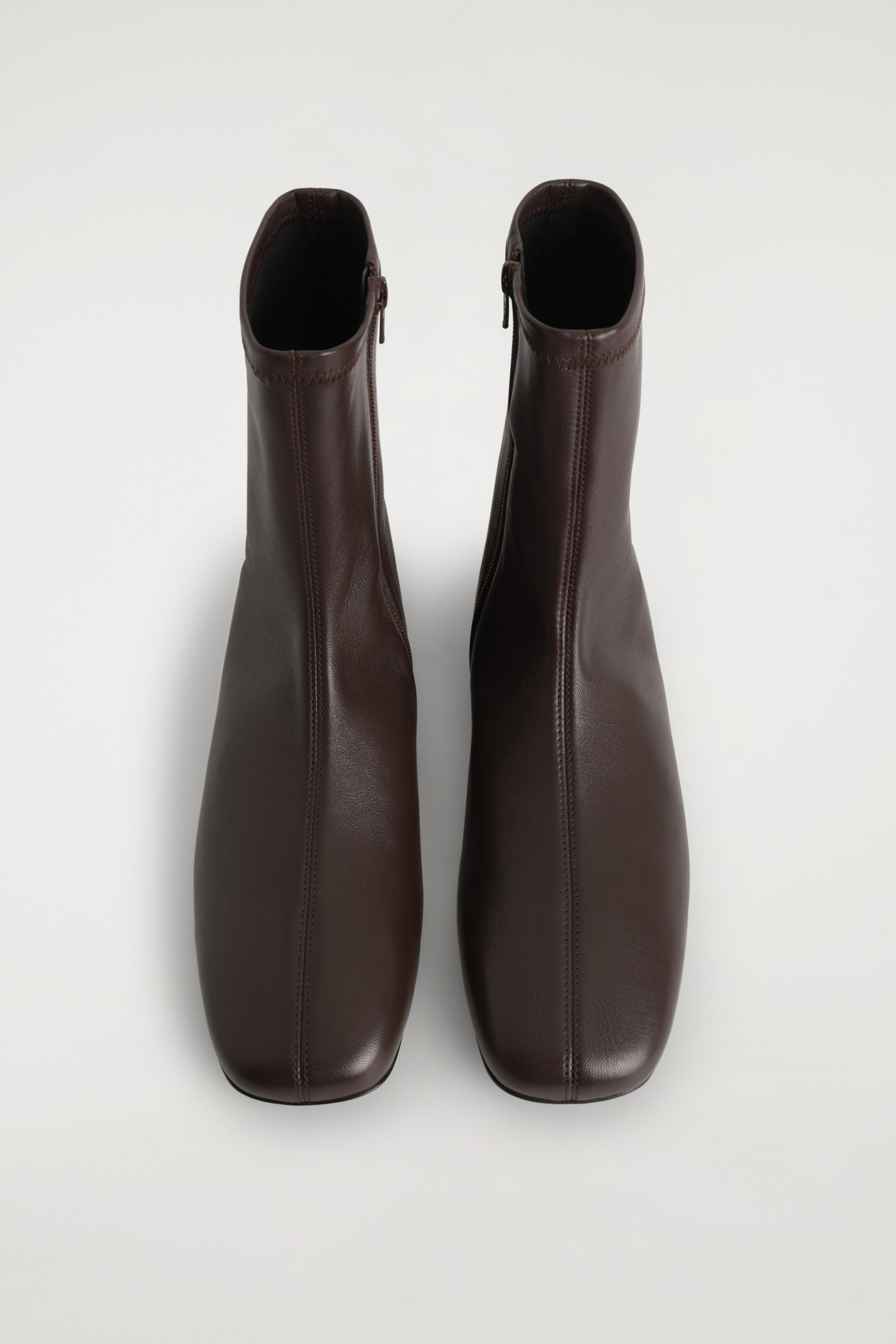 View larger image: A pair of dark brown leather sock boots is presented from a TOP angle, each featuring a smooth texture, rounded square toes, and a slim silhouette with a central vertical seam. A metal zipper is visible along the inner side of each boot's shaft.