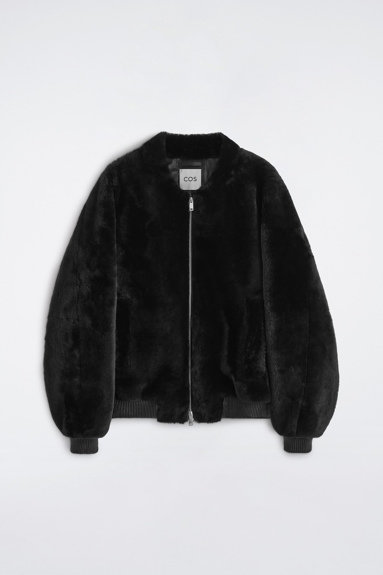 A black padded shearling bomber jacket is shown from the front, highlighting its plush, textured exterior and relaxed silhouette. It features a silver-tone front zipper closure, along with ribbed knit cuffs and a matching ribbed hem.