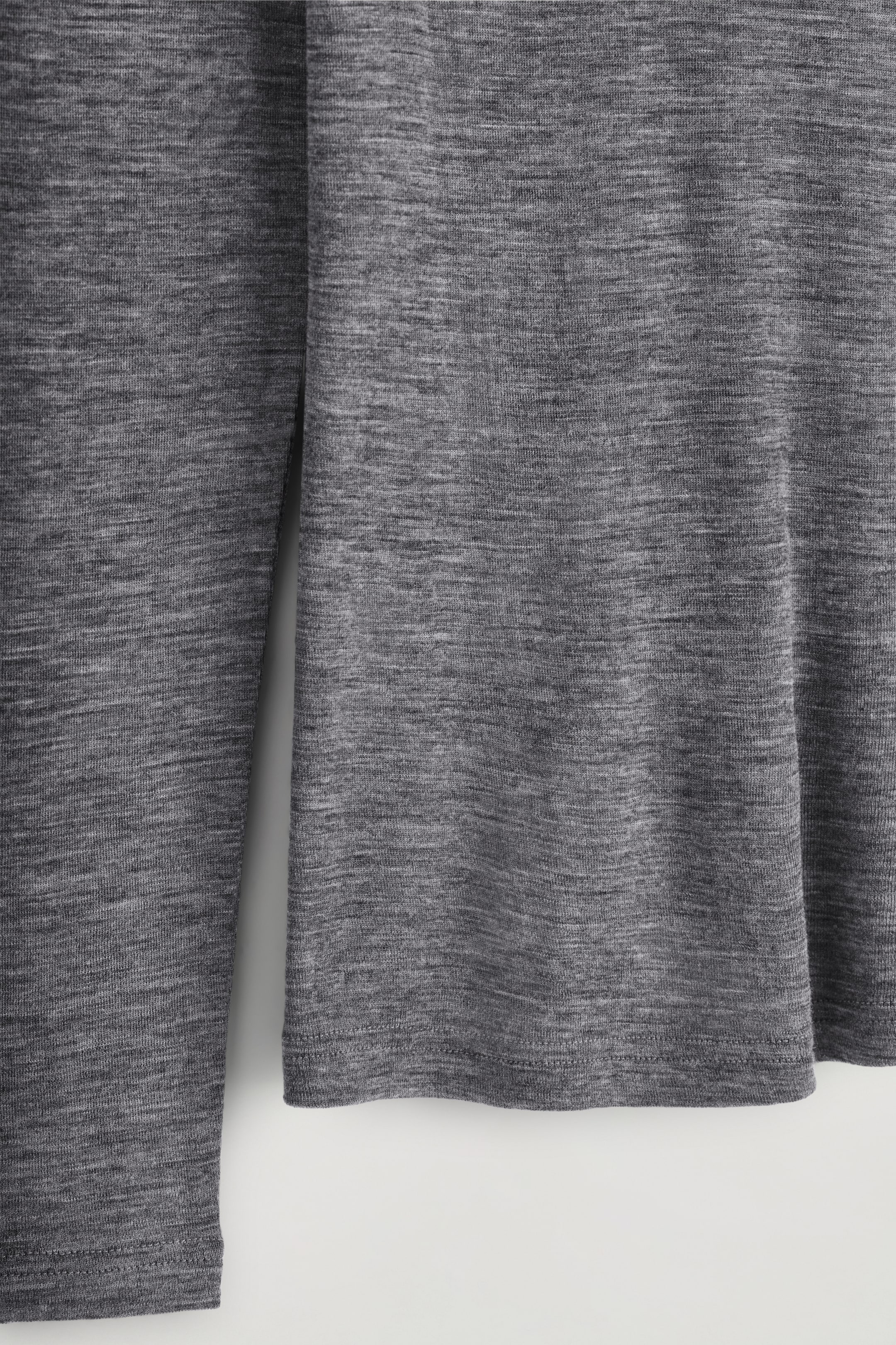 Grösseres Bild ansehen: Ein graues Melange-Langarmshirt wird präsentiert, das seine fein gestrickte Textur und schlicht genähte Säume am Körper und an den Ärmeln zeigt.