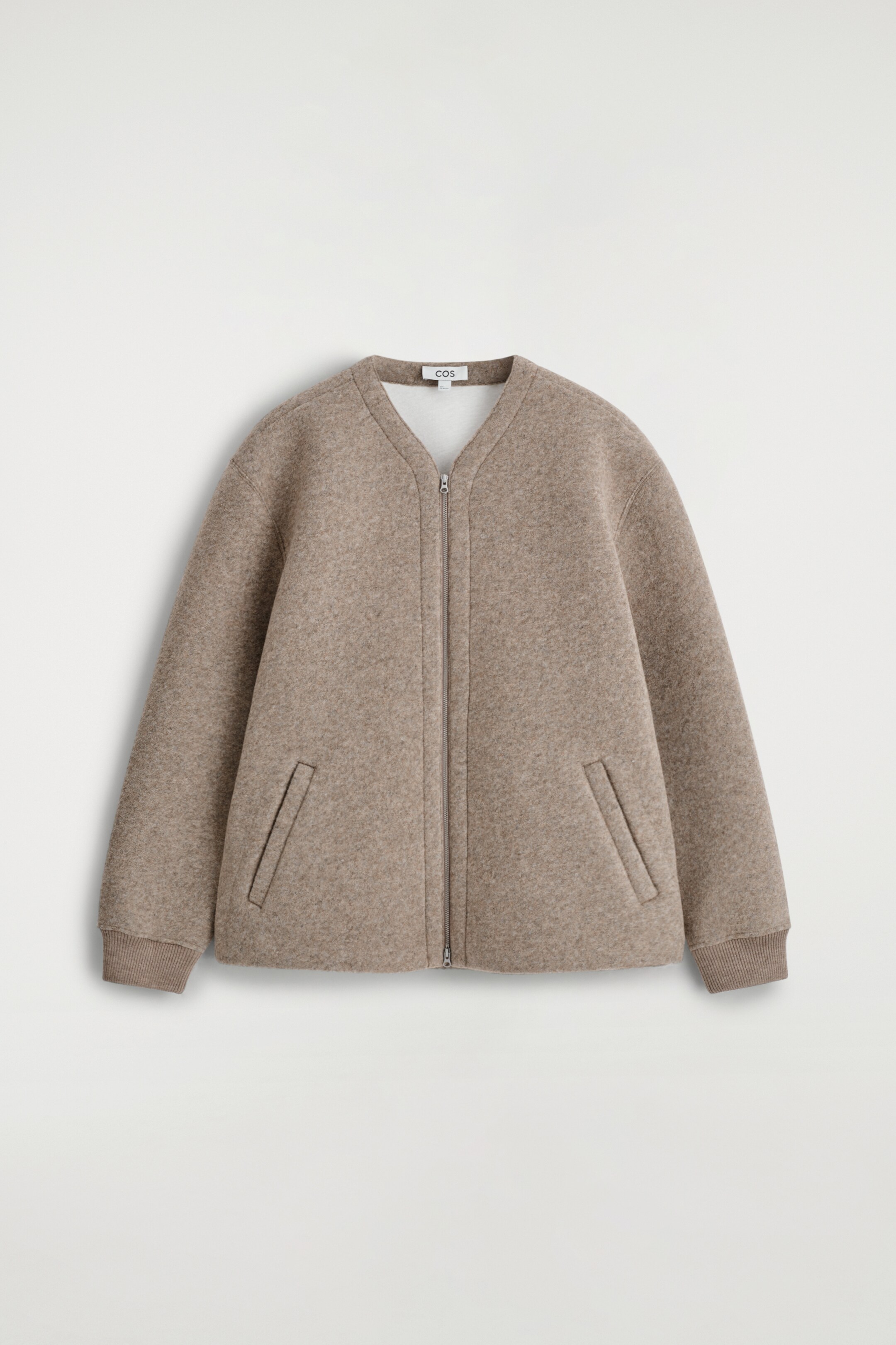 Agrandir l'image: Une veste taupe sans col avec une texture feutrée est présentée de face, dotée d'une fermeture éclair sur toute la longueur, de deux poches passepoilées en biais et de poignets côtelés.