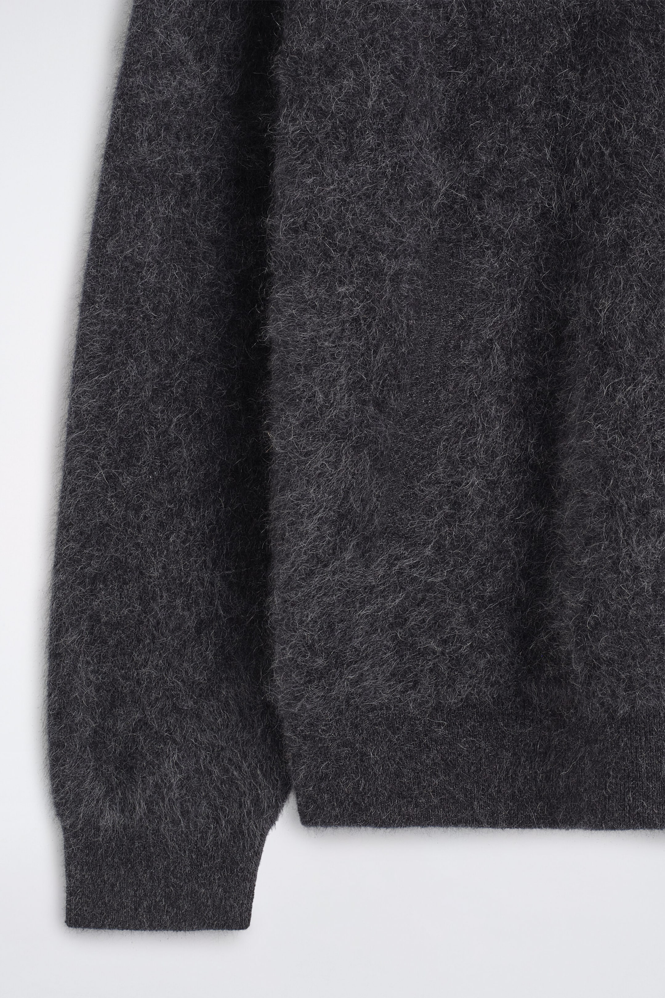 The dark gray brushed pure cashmere hoodie is shown in close-up, highlighting its soft, fuzzy texture. The image details the ribbed sleeve cuff and the matching ribbed hem at the bottom of the garment.