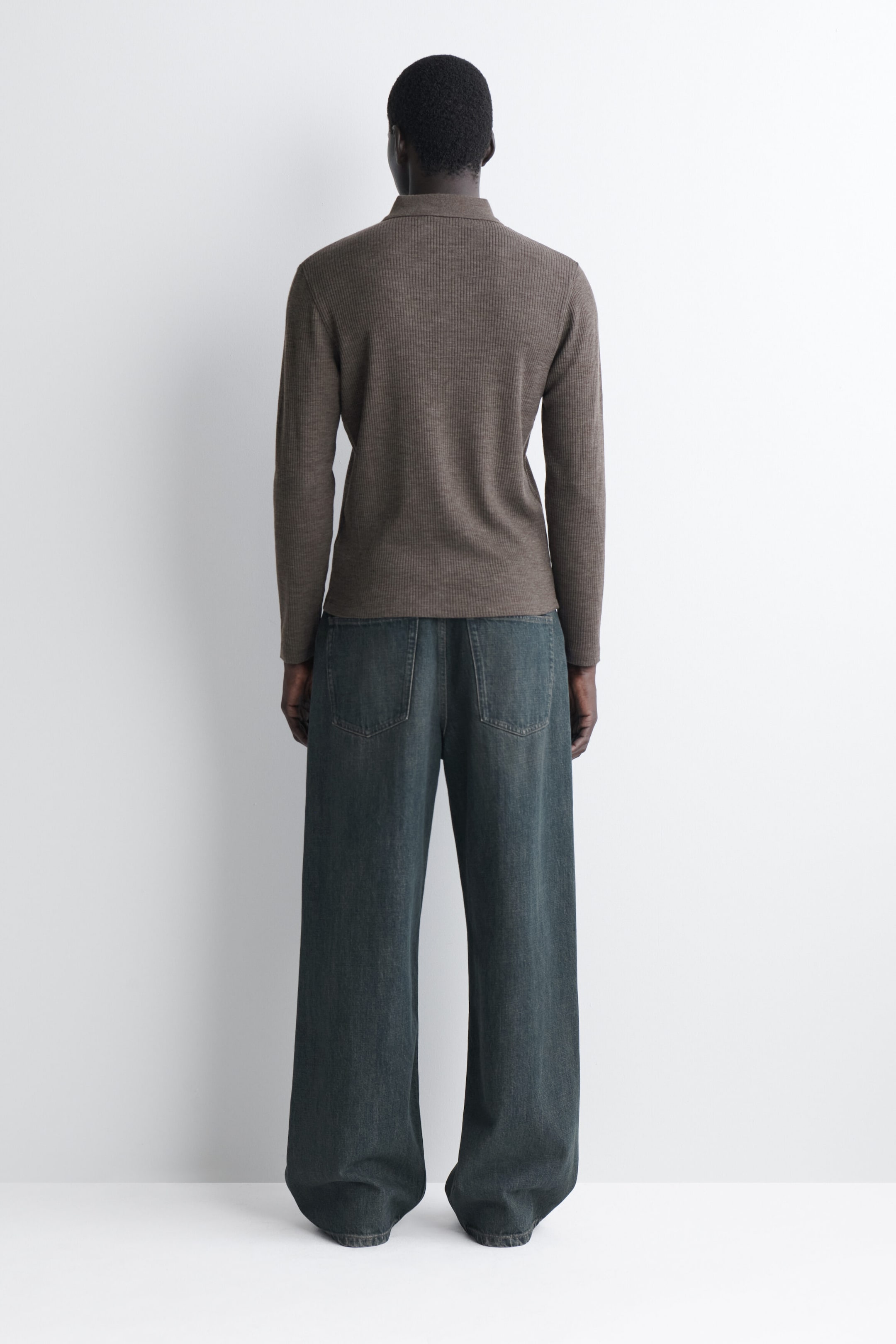 Das schmale, gerippte Wollshirt wird von hinten gezeigt und präsentiert seine feine Rippstrickstruktur, die langen Ärmel und den Polokragen. Das taupefarbene Shirt liegt körpernah an und endet auf Hüfthöhe; es wird zusammen mit Jeans mit weitem Bein gestylt, um seine schmale Silhouette zu betonen. Das schmale, gerippte Wollshirt wird von hinten gezeigt und präsentiert seine feine Rippstrickstruktur, die langen Ärmel und den Polokragen. Das taupefarbene Shirt liegt körpernah an und endet auf Hüfthöhe; es wird zusammen mit Jeans mit weitem Bein gestylt, um seine schmale Silhouette zu betonen.