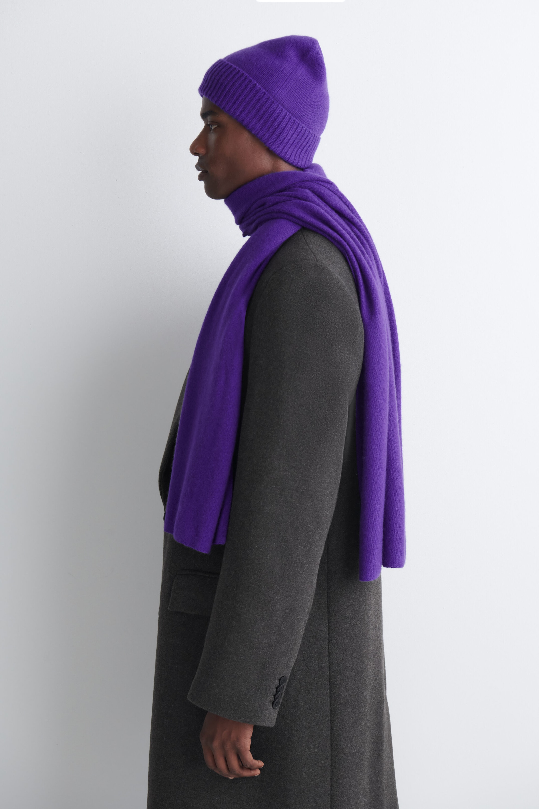 A purple cashmere scarf is worn wrapped around the model’s neck, with one end draped over the shoulder and the other hanging down the front. The scarf is styled over a dark gray wool coat and paired with a matching purple knit beanie. A purple cashmere scarf is worn wrapped around the model’s neck, with one end draped over the shoulder and the other hanging down the front. The scarf is styled over a dark gray wool coat and paired with a matching purple knit beanie.