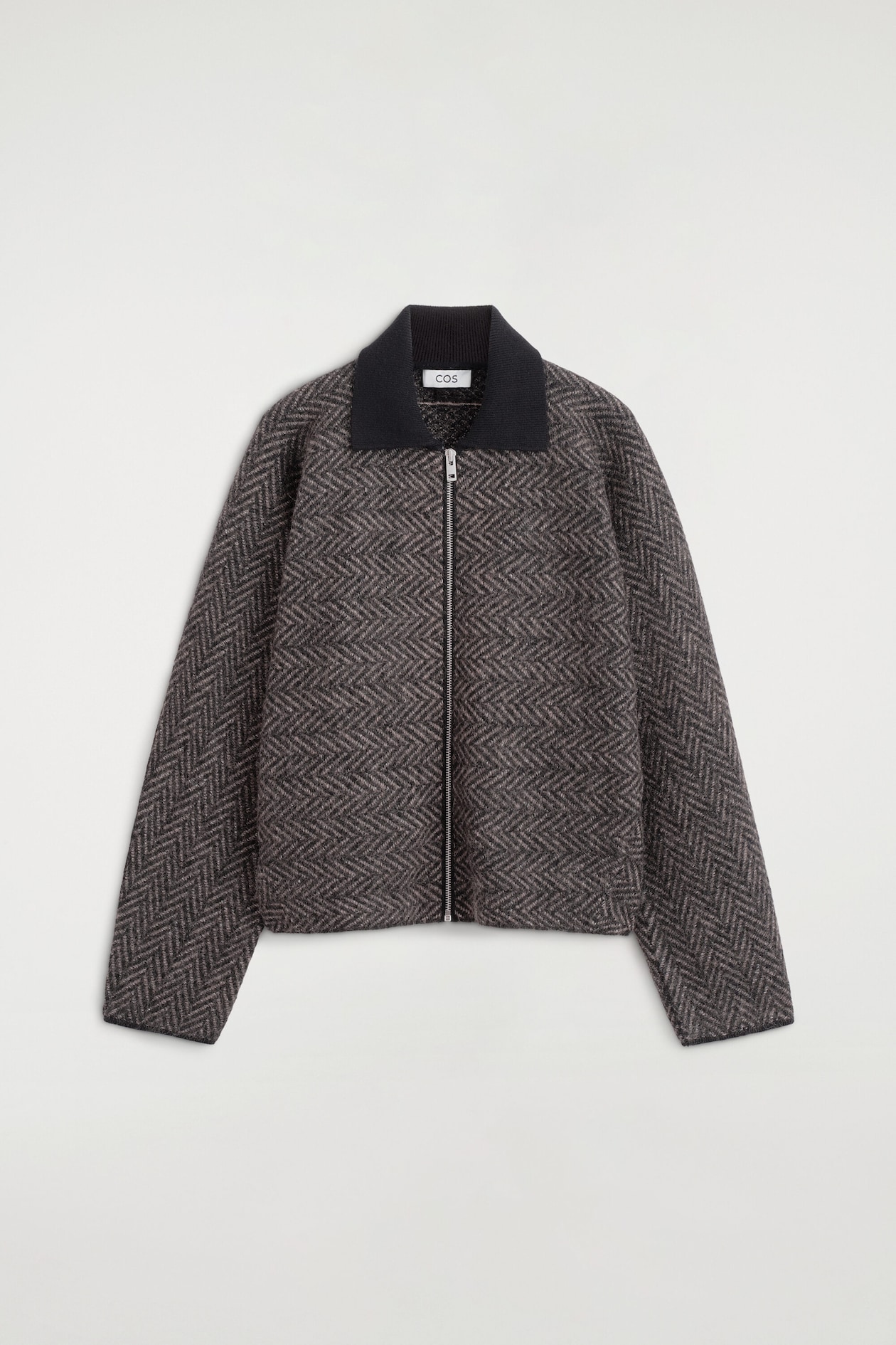 Une veste en tricot à motif chevron dans des tons de brun et de gris est présentée de face, avec un col côtelé noir contrastant et une fermeture éclair centrale de couleur argentée. La veste à coupe décontractée présente des manches longues et un ourlet droit.