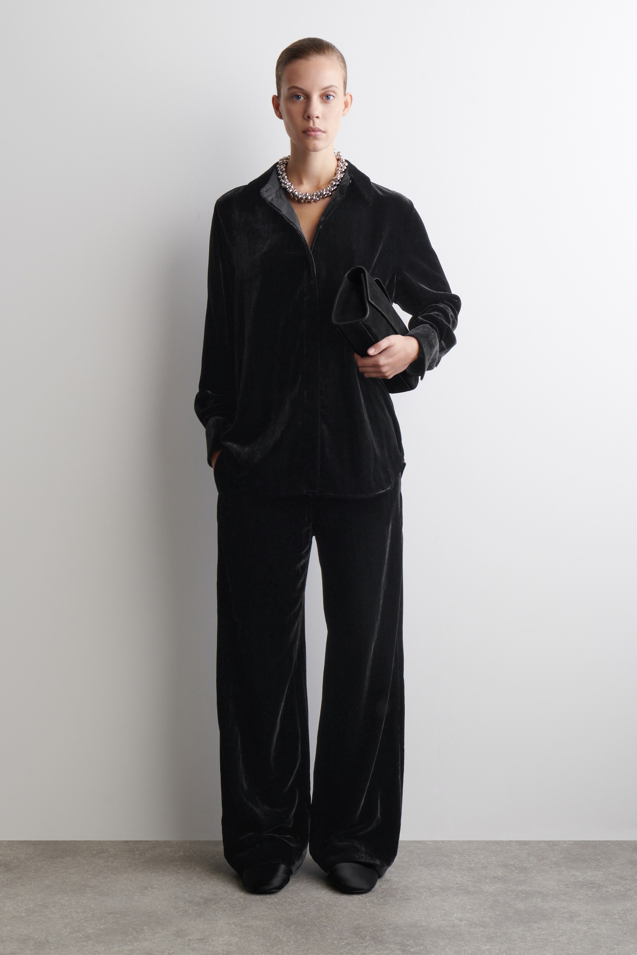 Agrandir l'image: Une chemise en velours noir et un pantalon à jambes larges assorti sont présentés de face. La chemise à manches longues, en velours doux et scintillant, présente une coupe décontractée et un col souple, tandis que le pantalon pleine longueur offre une coupe ample et fluide.