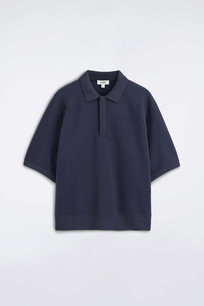 Das marineblaue Scuba-Jersey-Poloshirt ist von vorne zu sehen und verfÃ¼gt Ã¼ber einen Rippkragen, eine verdeckte Knopfleiste sowie kurze RaglanÃ¤rmel mit RippbÃ¼ndchen. Das KleidungsstÃ¼ck prÃ¤sentiert eine entspannte, strukturierte Silhouette mit einem breiten Rippbund. - 1