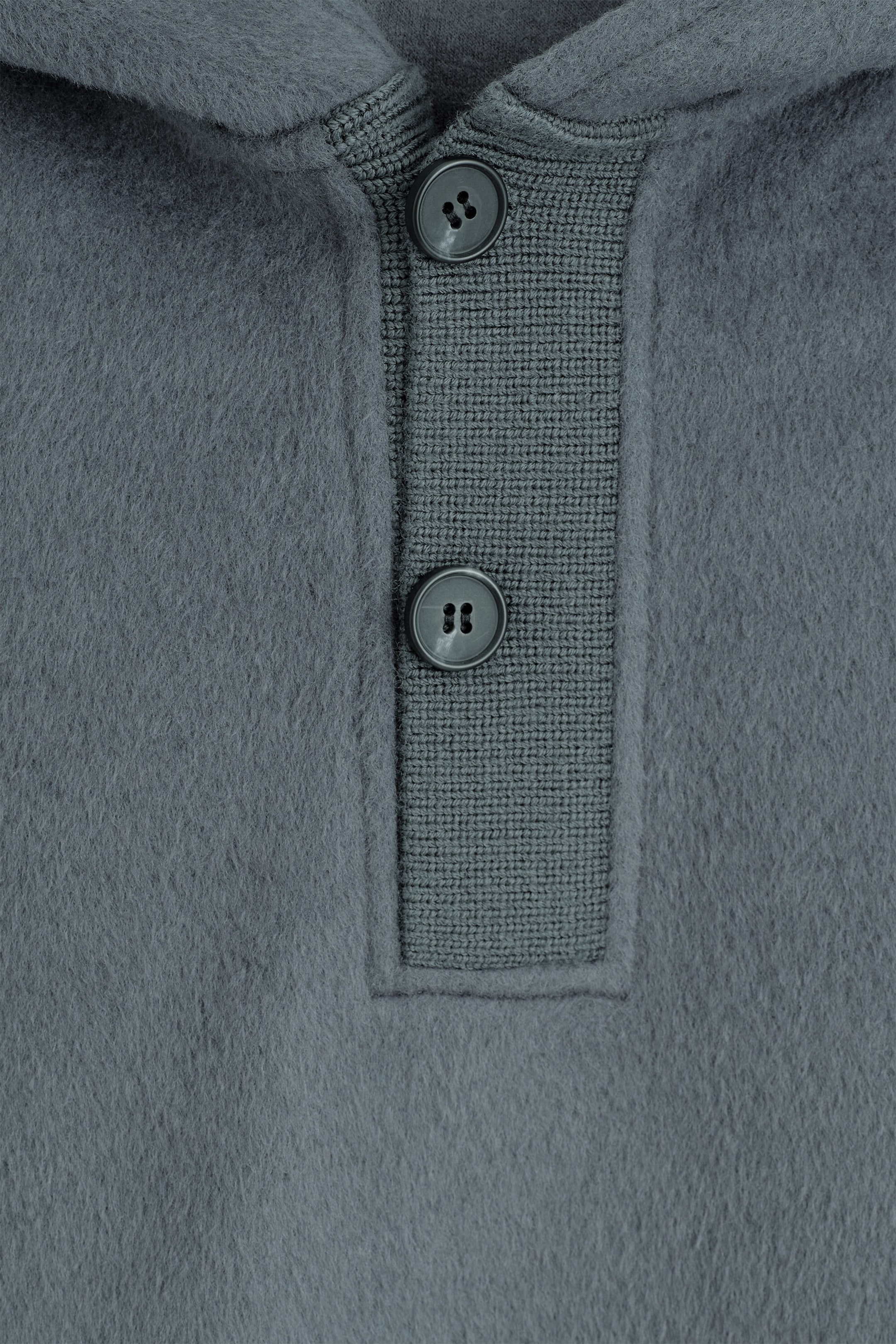 Un gros plan de face d’un chandail à capuchon gris mettant en valeur sa texture brossée et duveteuse, ainsi qu’une patte Henley en tricot côtelé avec deux boutons foncés. Un gros plan de face d’un chandail à capuchon gris mettant en valeur sa texture brossée et duveteuse, ainsi qu’une patte Henley en tricot côtelé avec deux boutons foncés.