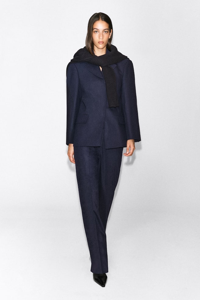 Ein marineblauer Blazer aus Wollmischung mit strukturierten Schultern und Pattentaschen wird vom Model als Teil eines Anzugs mit passender Hose getragen. Das Outfit wird mit einem schwarzen Strickschal gestylt, der über die Schultern gelegt ist. - 1