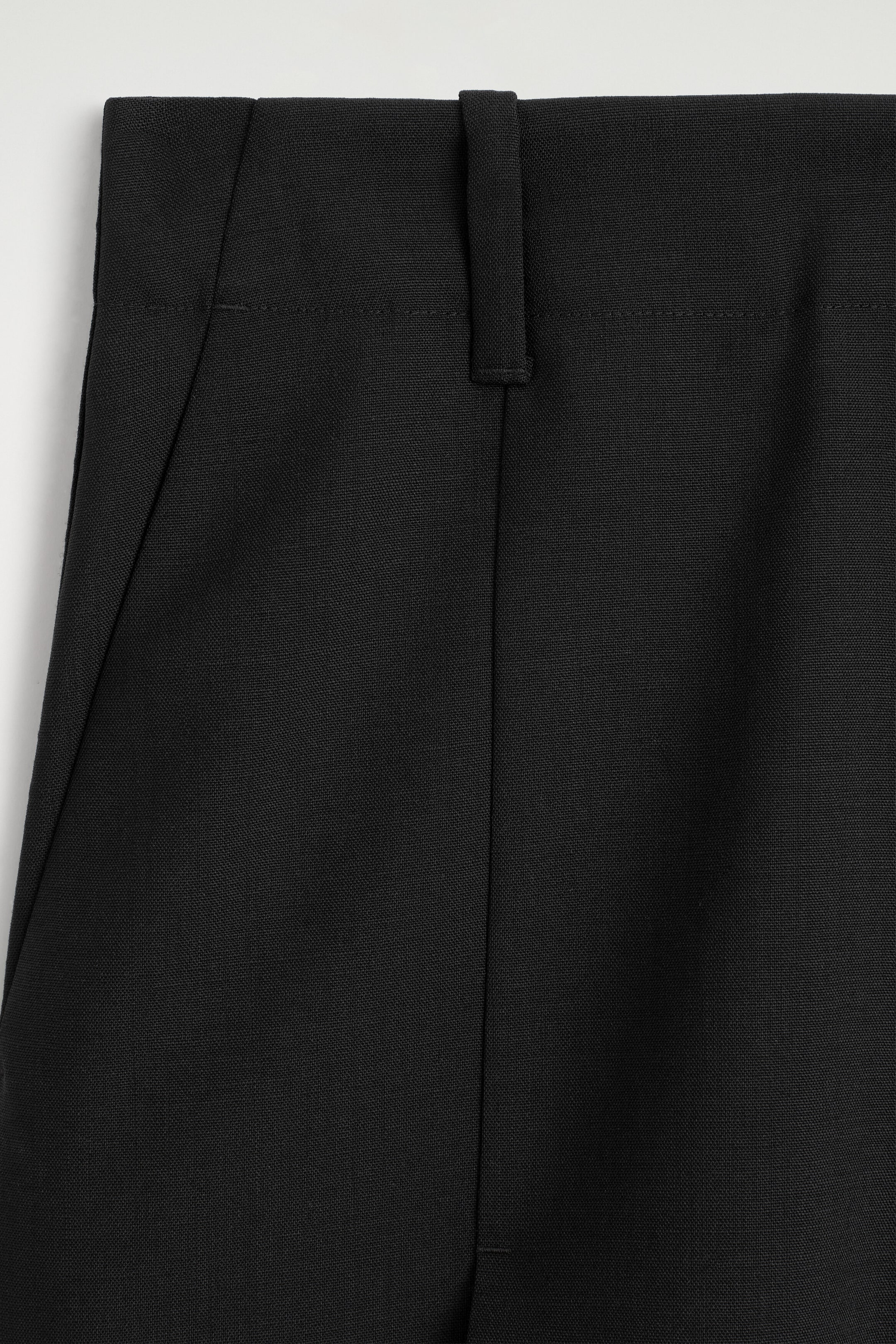 The BOX-PLEAT CHECKED WOOL MIDI SKIRT is shown from the upper front, featuring a structured black fabric waistband with visible stitching along the top and bottom edges. A single belt loop is positioned on the right, and a subtle diagonal seam is visible on the left. The BOX-PLEAT CHECKED WOOL MIDI SKIRT is shown from the upper front, featuring a structured black fabric waistband with visible stitching along the top and bottom edges. A single belt loop is positioned on the right, and a subtle diagonal seam is visible on the left.