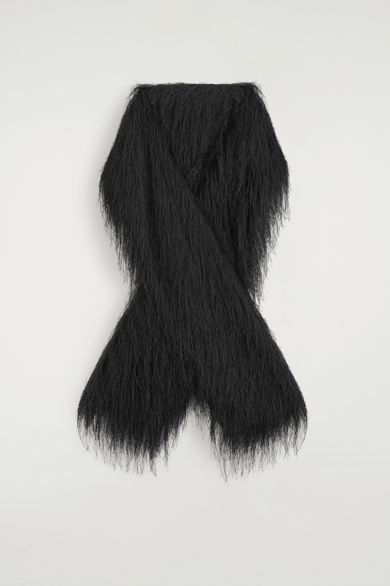 A black scarf is hanging in a front-facing view, draped in a crossed-over arrangement. Long, wispy fringe covers the entire surface of the scarf, creating a dense, textured appearance.