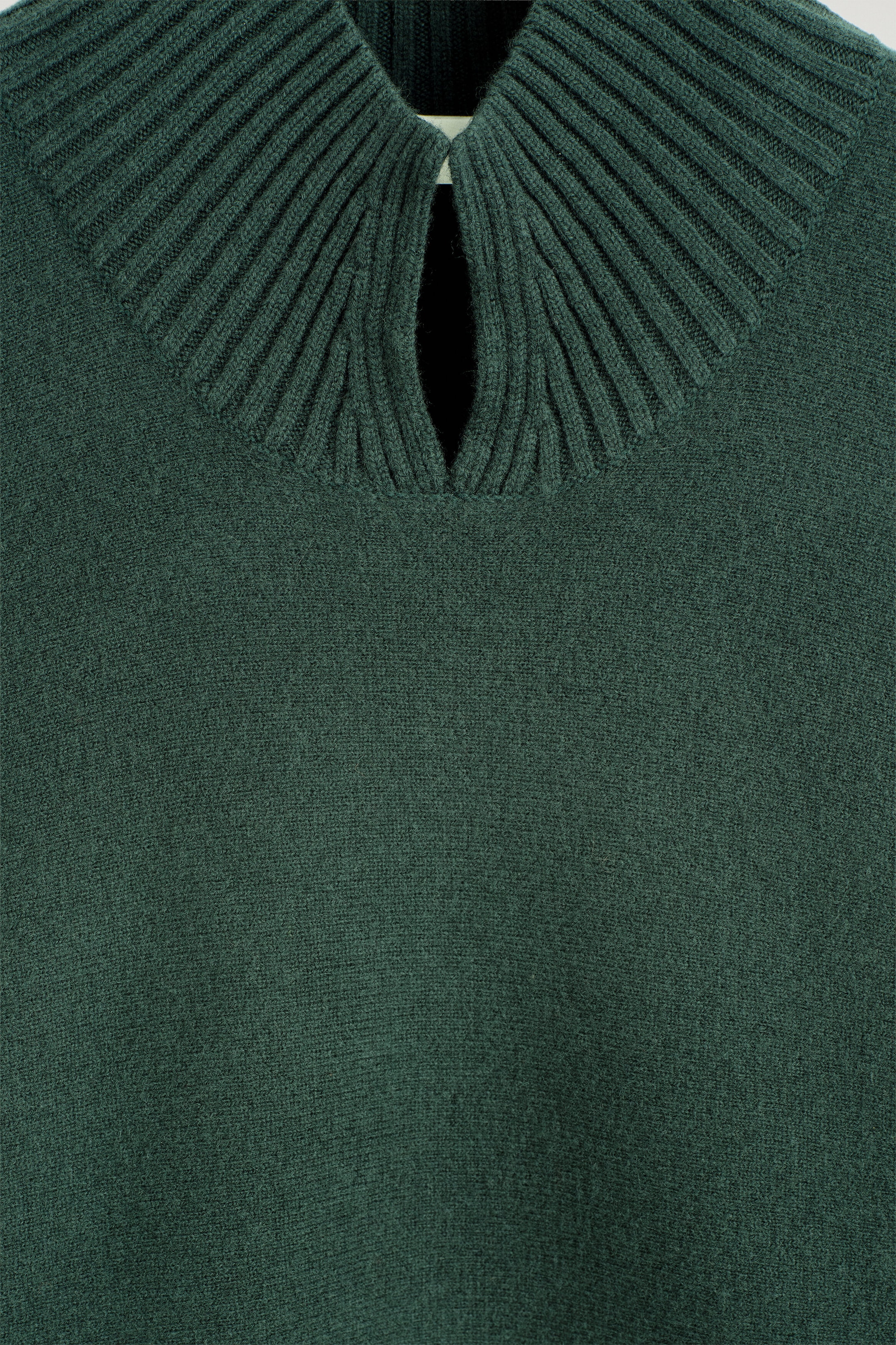 Gros plan d’un chandail en maille vert foncé montrant l’encolure avant, avec un large col côtelé qui se rejoint pour former une ouverture centrale en forme de goutte. Le chandail présente une texture à mailles fines sur l’ensemble du corps principal sous le col côtelé. Gros plan d’un chandail en maille vert foncé montrant l’encolure avant, avec un large col côtelé qui se rejoint pour former une ouverture centrale en forme de goutte. Le chandail présente une texture à mailles fines sur l’ensemble du corps principal sous le col côtelé.