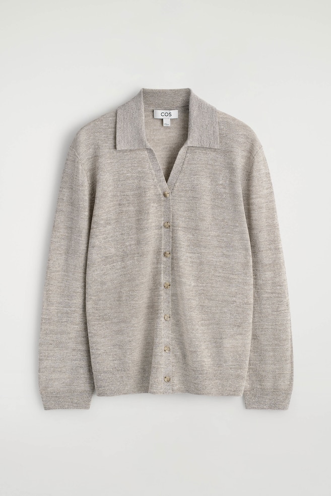 Un cardigan polo lavorato a maglia in mélange beige chiaro mostra il DAVANTI, con colletto aperto e chiusura frontale con sette piccoli bottoni rotondi color marrone chiaro. Presenta maniche lunghe con polsini a coste e orlo a coste. - 1
