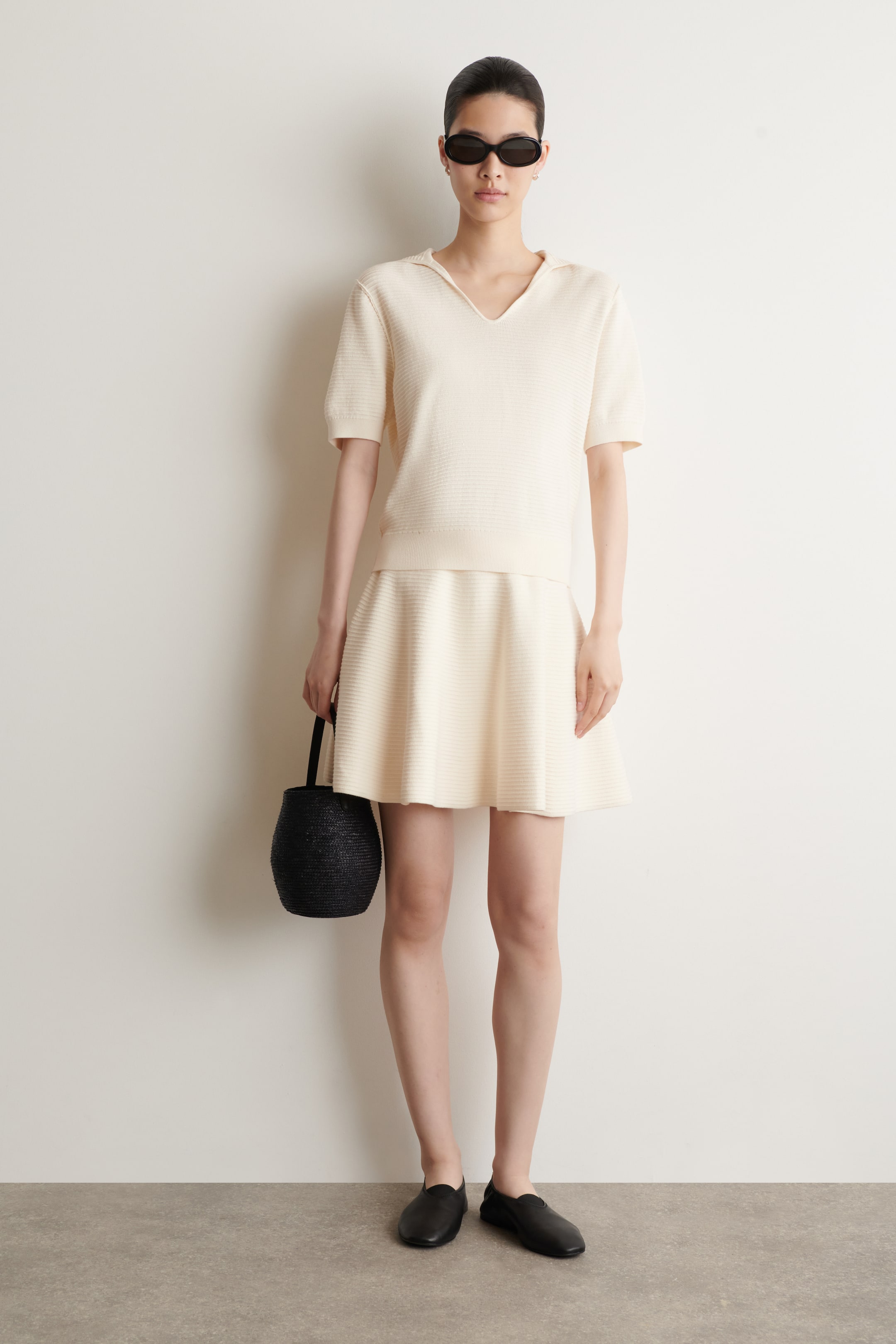 View larger image: A cream knit set presents a short-sleeved polo top and an A-line mini skirt, both showcasing a subtle horizontal textured knit pattern. The top features a pointed collar, V-neckline, ribbed cuffs, and a ribbed hem, while the skirt includes a ribbed waistband.