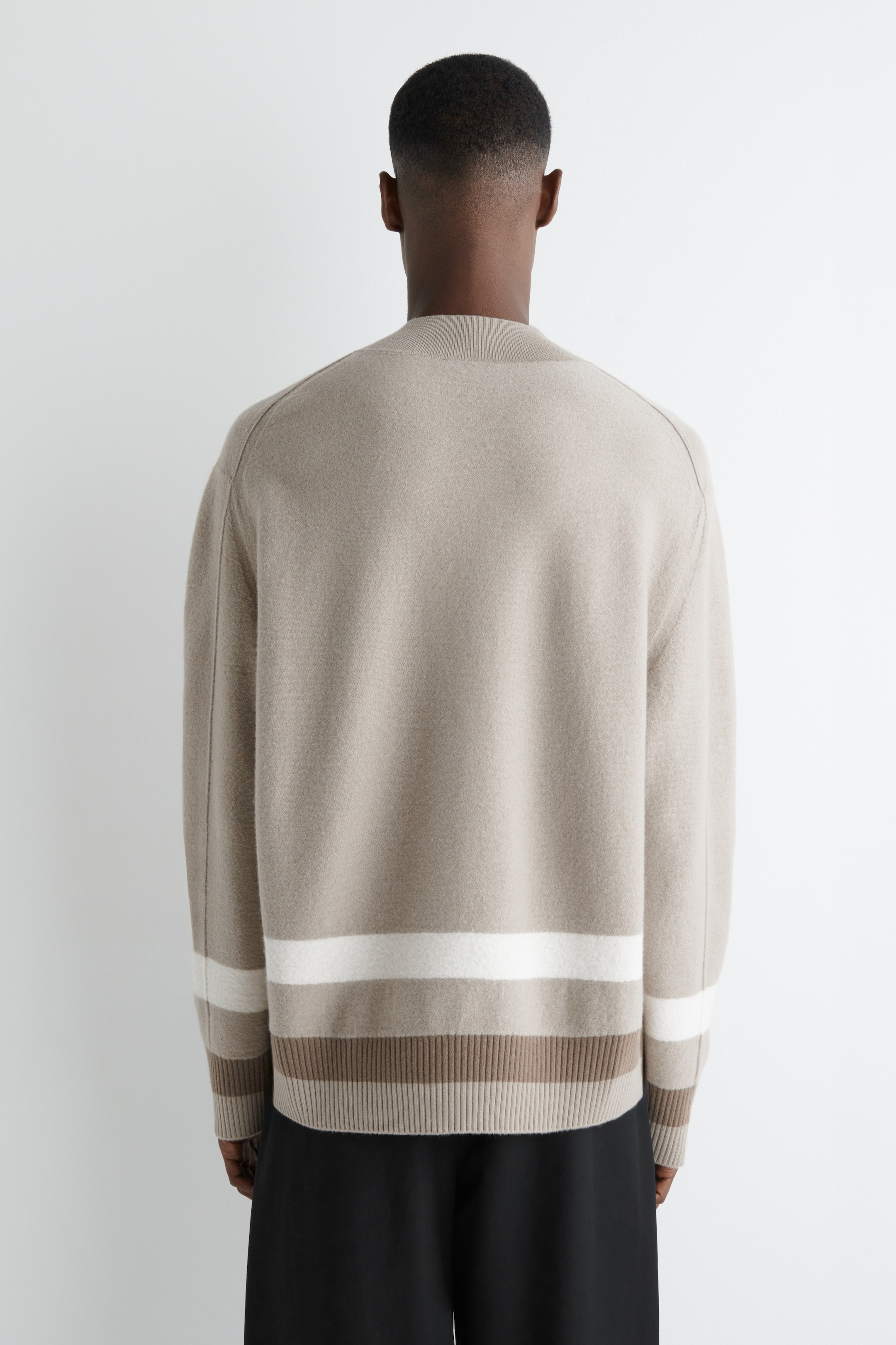 View larger image: A beige knit sweater is being viewed from the back, featuring raglan sleeves, while horizontal stripes are running across the lower body and lower sleeves. A wide white stripe is being positioned above two narrower brown stripes, and a ribbed hem and ribbed cuffs are completing the design.
