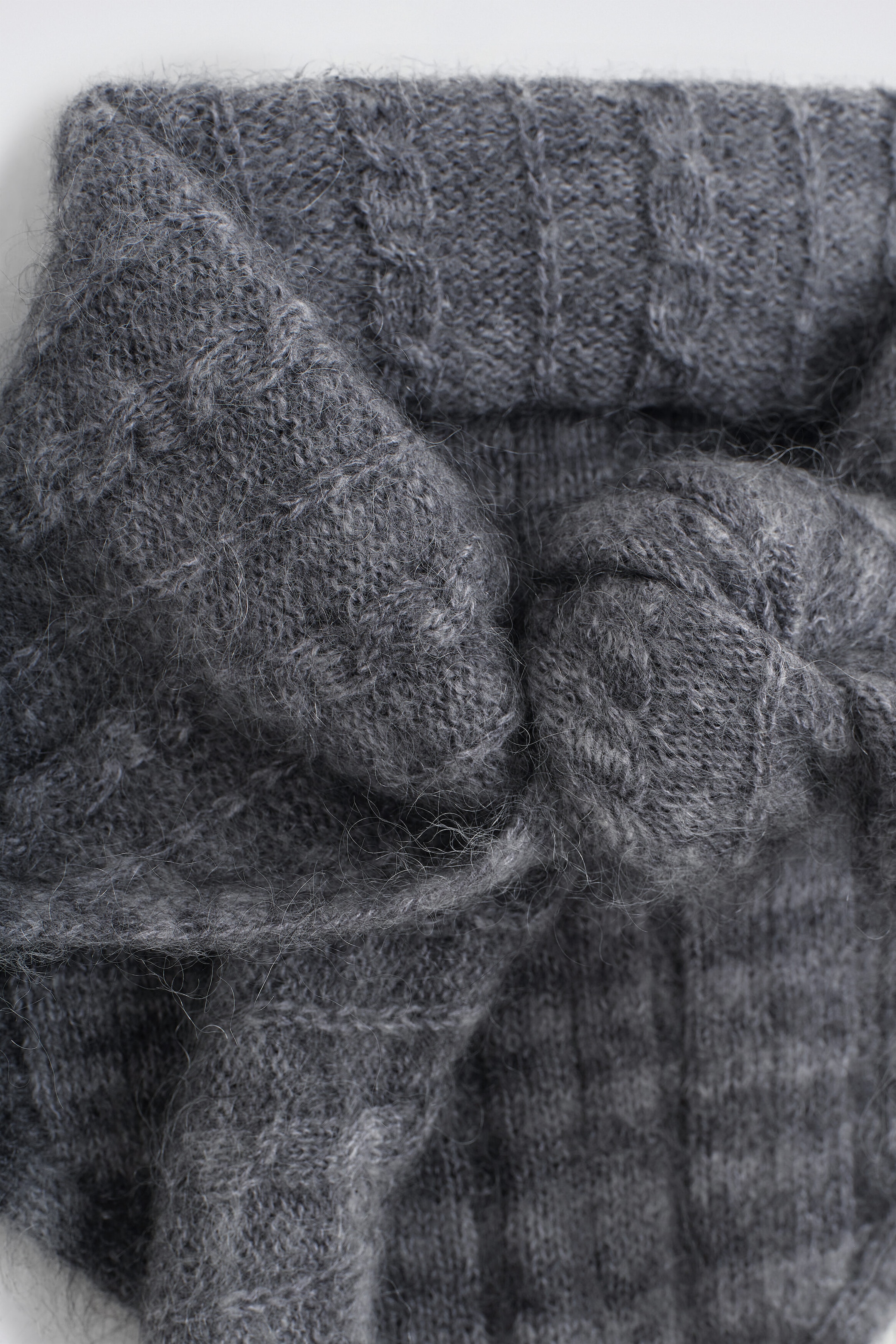 The checked cable-knit triangle scarf showcases a dark grey, fuzzy knit texture with a soft, brushed finish. It features intricate cable-knit details and a subtle checked pattern, appearing loosely knotted to highlight its thick, textured drape. The checked cable-knit triangle scarf showcases a dark grey, fuzzy knit texture with a soft, brushed finish. It features intricate cable-knit details and a subtle checked pattern, appearing loosely knotted to highlight its thick, textured drape.