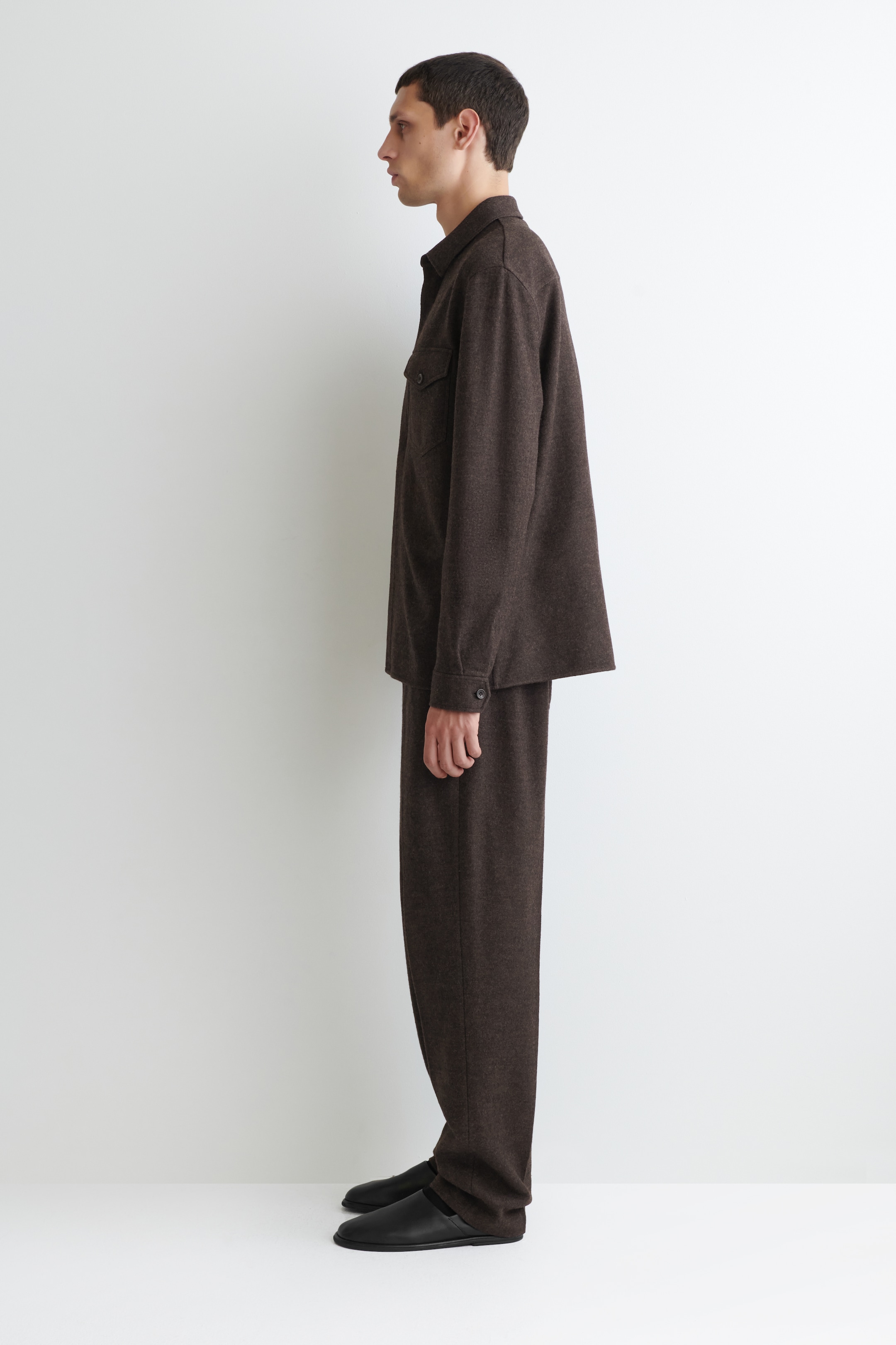Agrandir l'image: Un ensemble deux pièces marron foncé, vu de côté, présente une surchemise à coupe décontractée avec un col classique, deux poches poitrine à rabat et des poignets boutonnés. Le pantalon coordonné présente une coupe droite et décontractée.